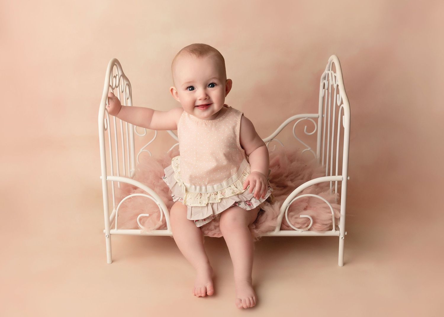 Baby sitting in white decorative metal bed frame against pink backdrop.Toowoomba Photographer Toowoomba Newborn Photographer