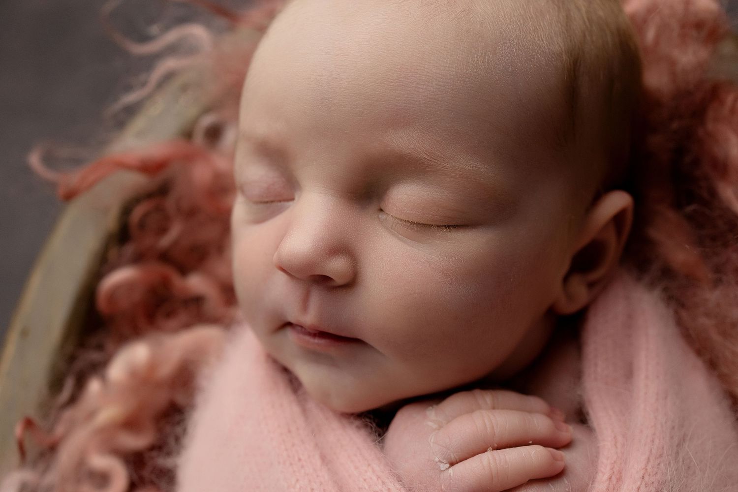 A sleeping newborn baby swaddled in soft pink fabric is photographed in a close-up series of peaceful poses.Toowoomba Photographer