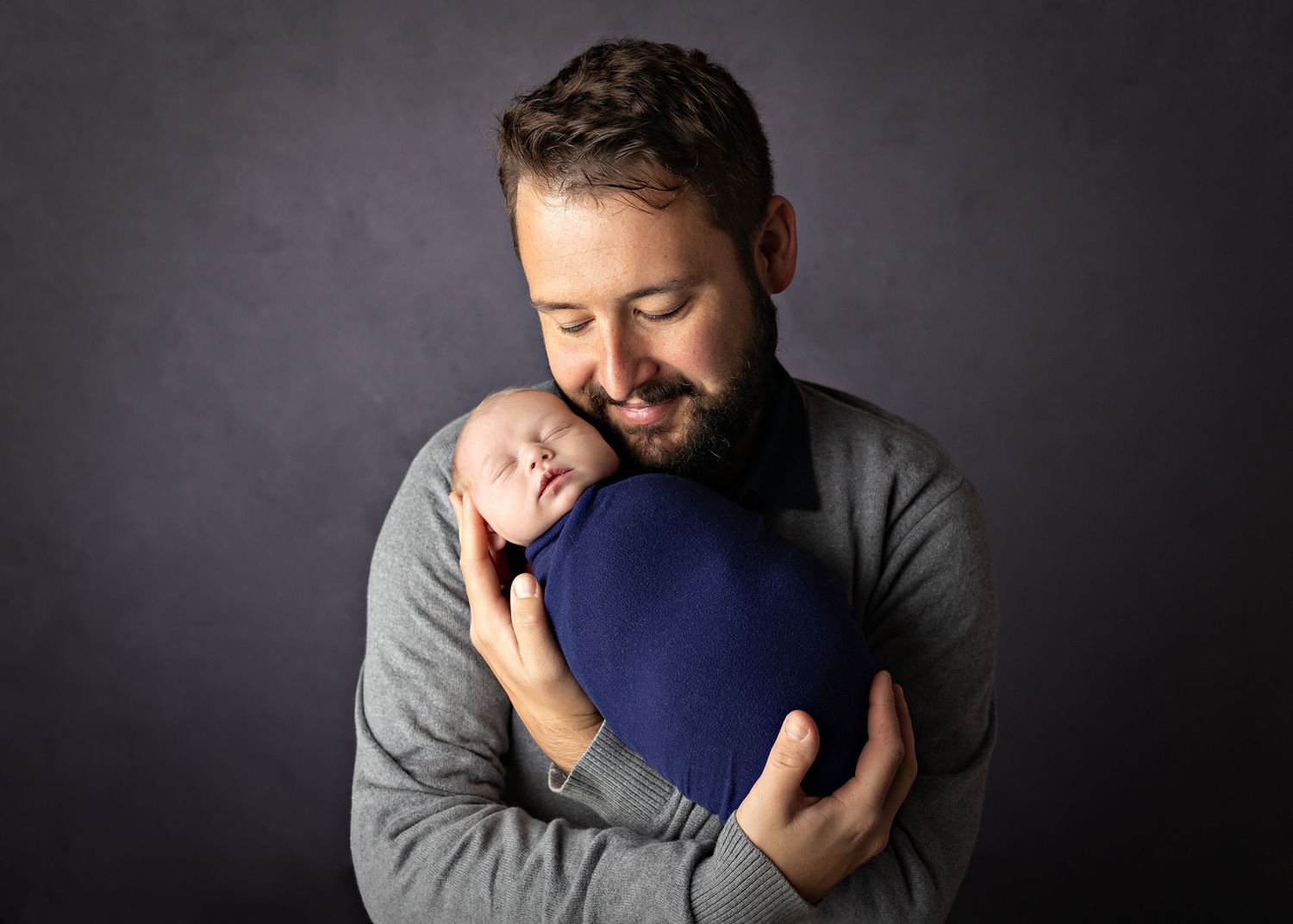 A tender moment captured between parent and newborn baby in a studio setting against a dark background.