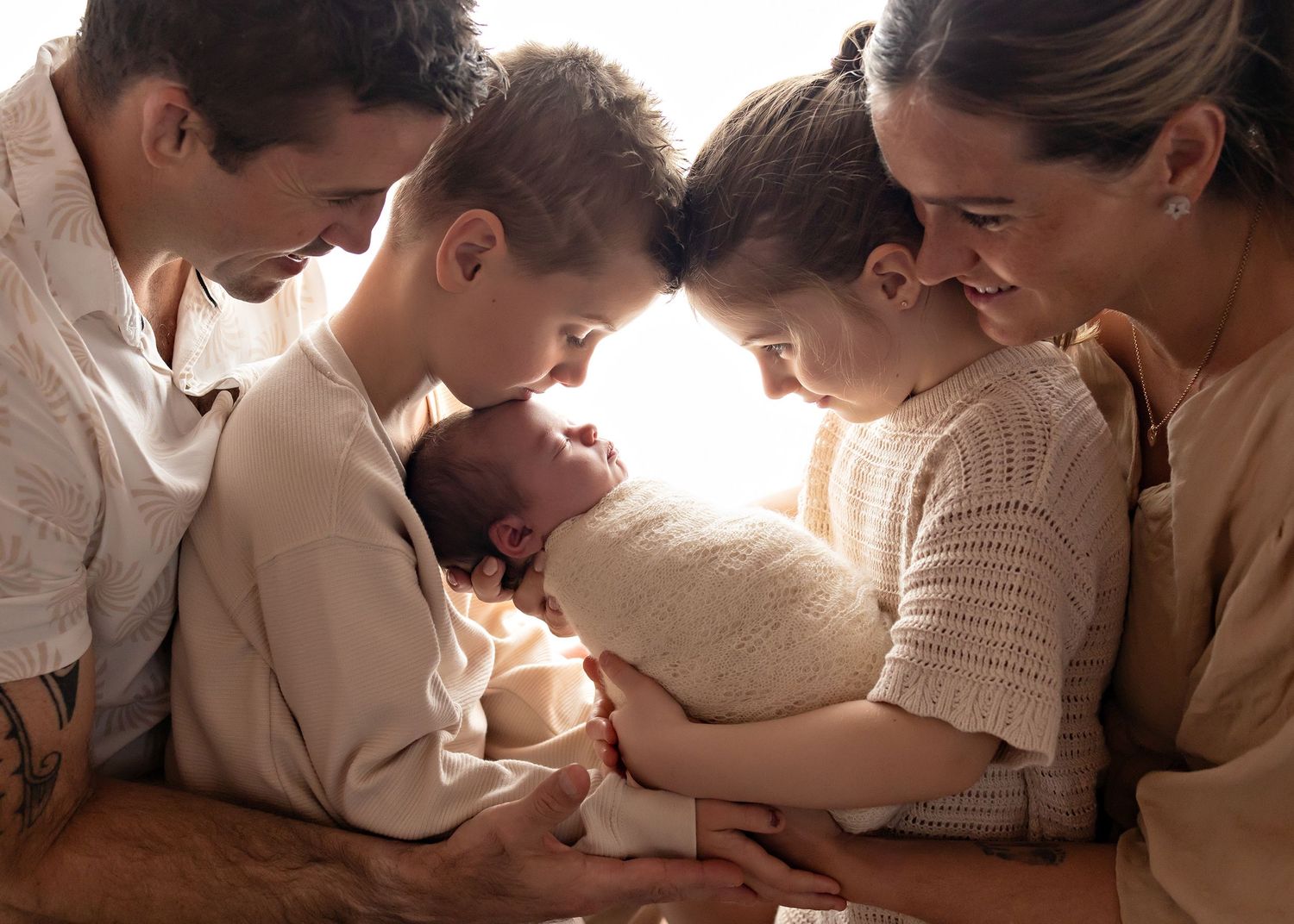 Family of four lovingly gazing at newborn baby wrapped in white, sharing a tender moment together.