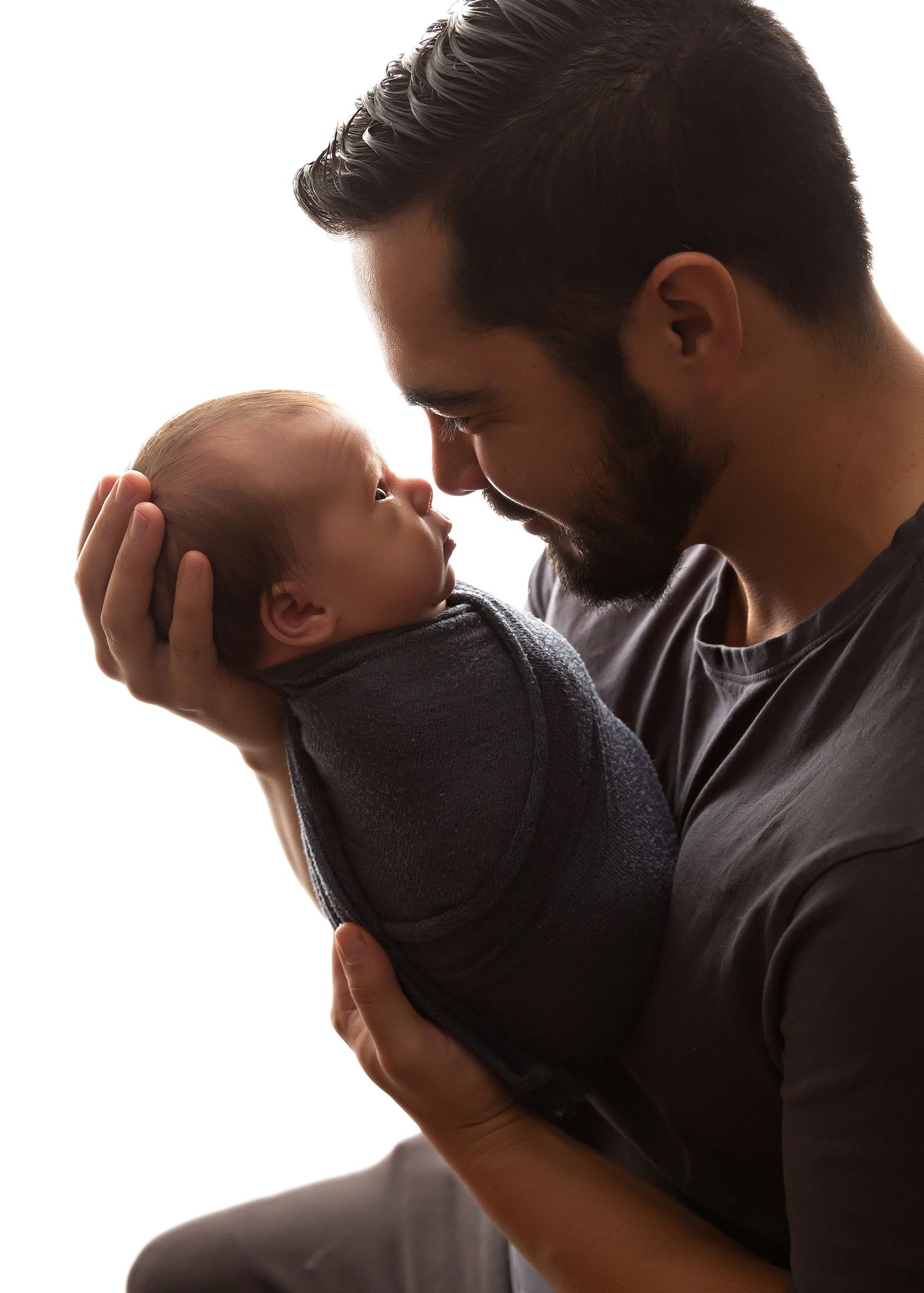 Silhouetted profile of parent tenderly holding newborn baby against bright background.