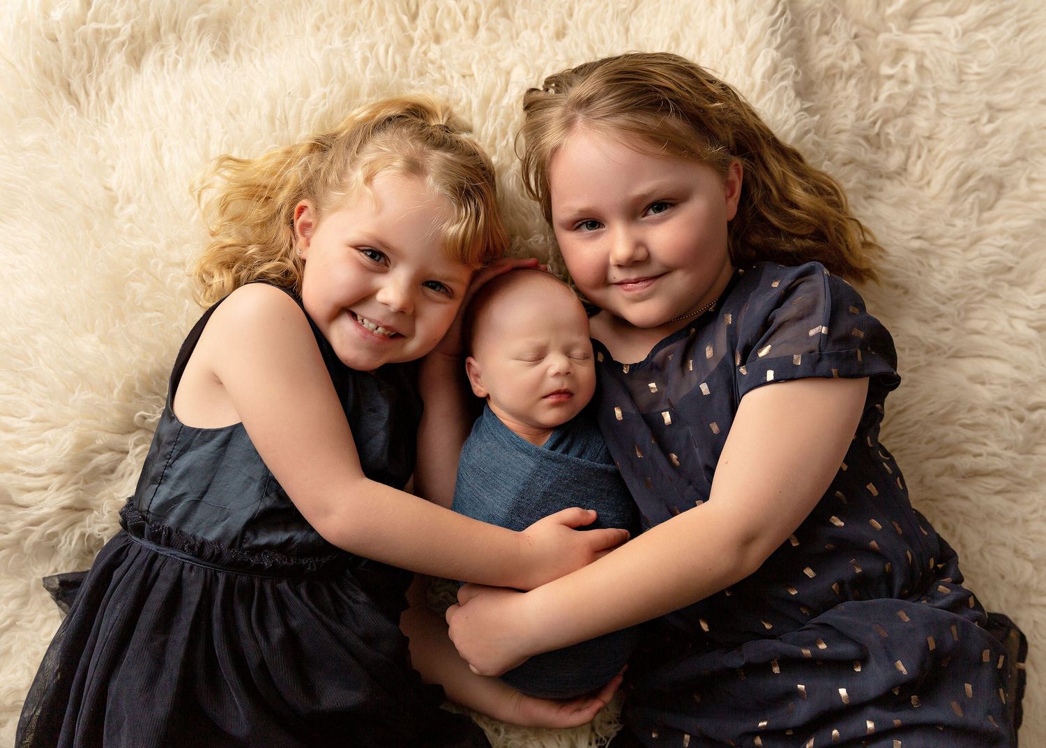 Children cuddling together on white fluffy carpet in coordinated navy and black outfits  Toowoomba Newborn Photographer