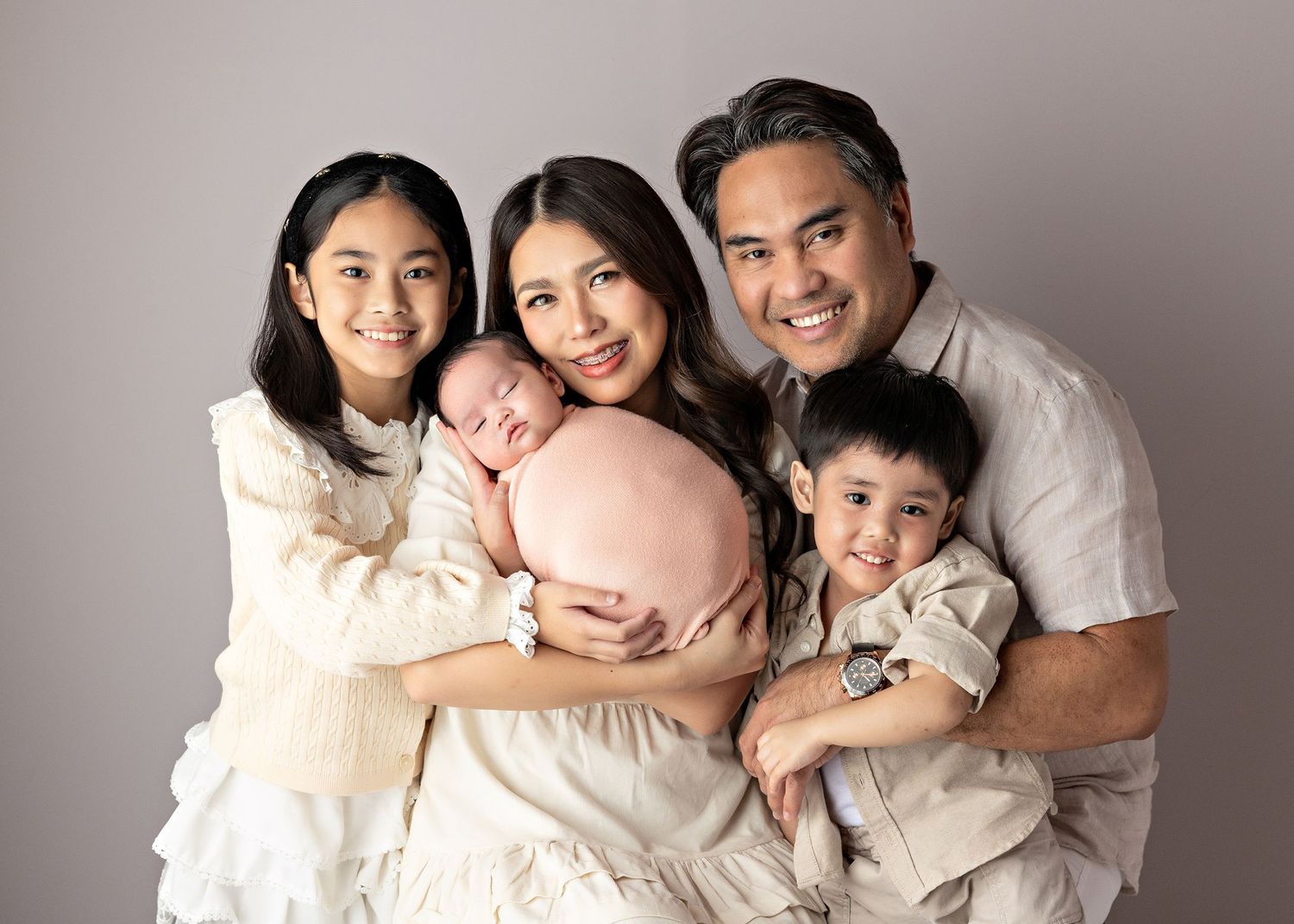Studio portrait of family in coordinated white outfits with newborn baby.