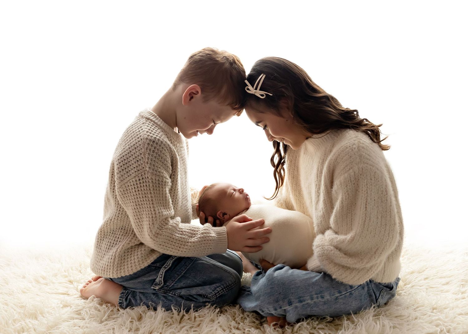 Cozy newborn photography session with baby and parent in cream sweaters on white carpet.