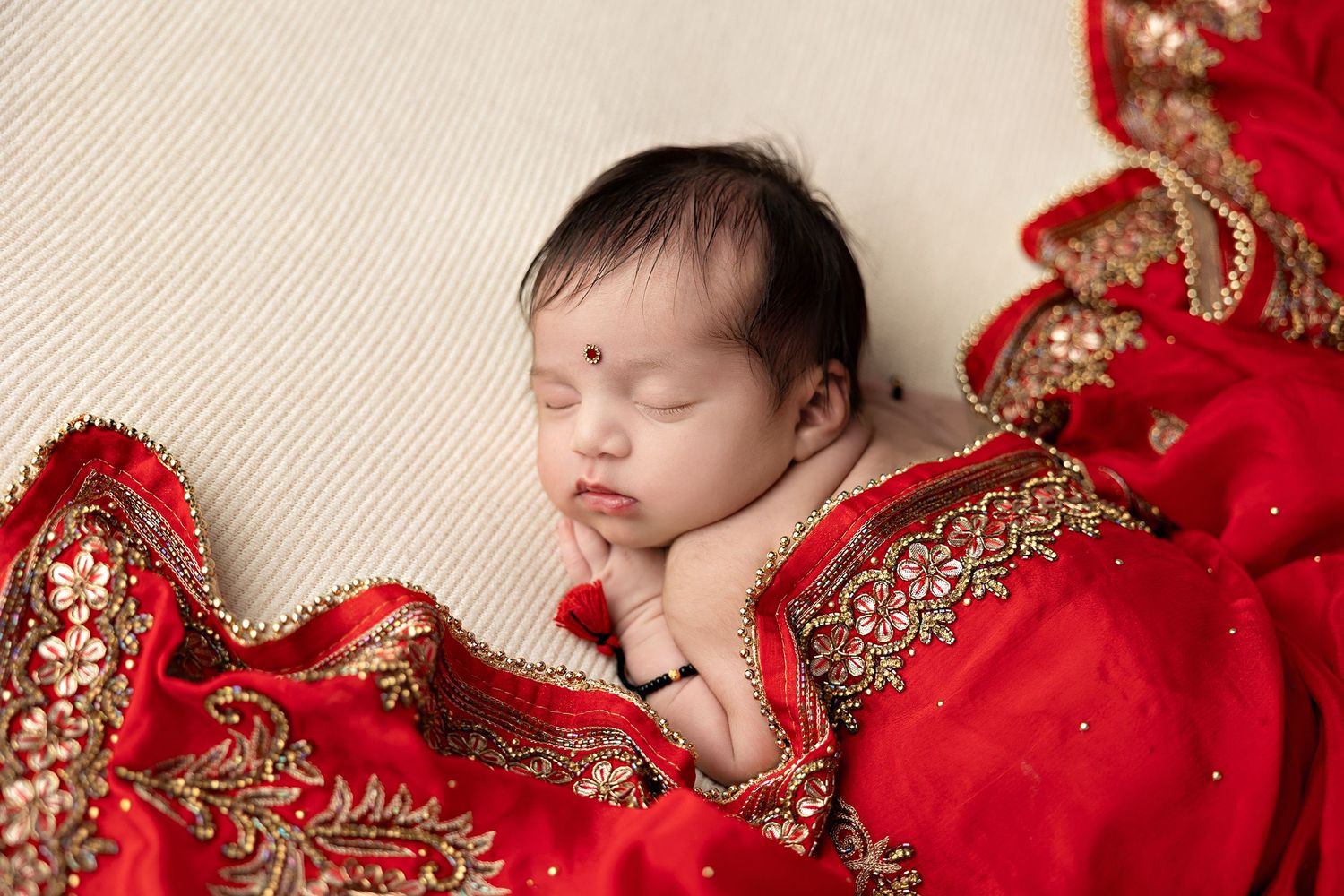 A sleeping newborn wrapped in luxurious red and gold fabric lies peacefully in a studio setting.Toowoomba Photographer