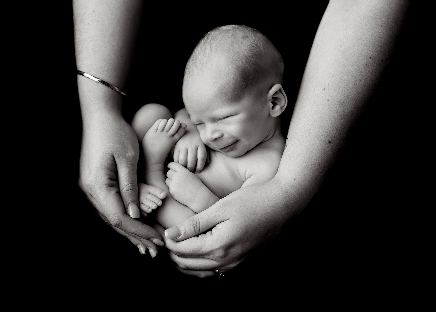 Black and white photo of a sleeping newborn baby cradled gently in the hands of two adults.