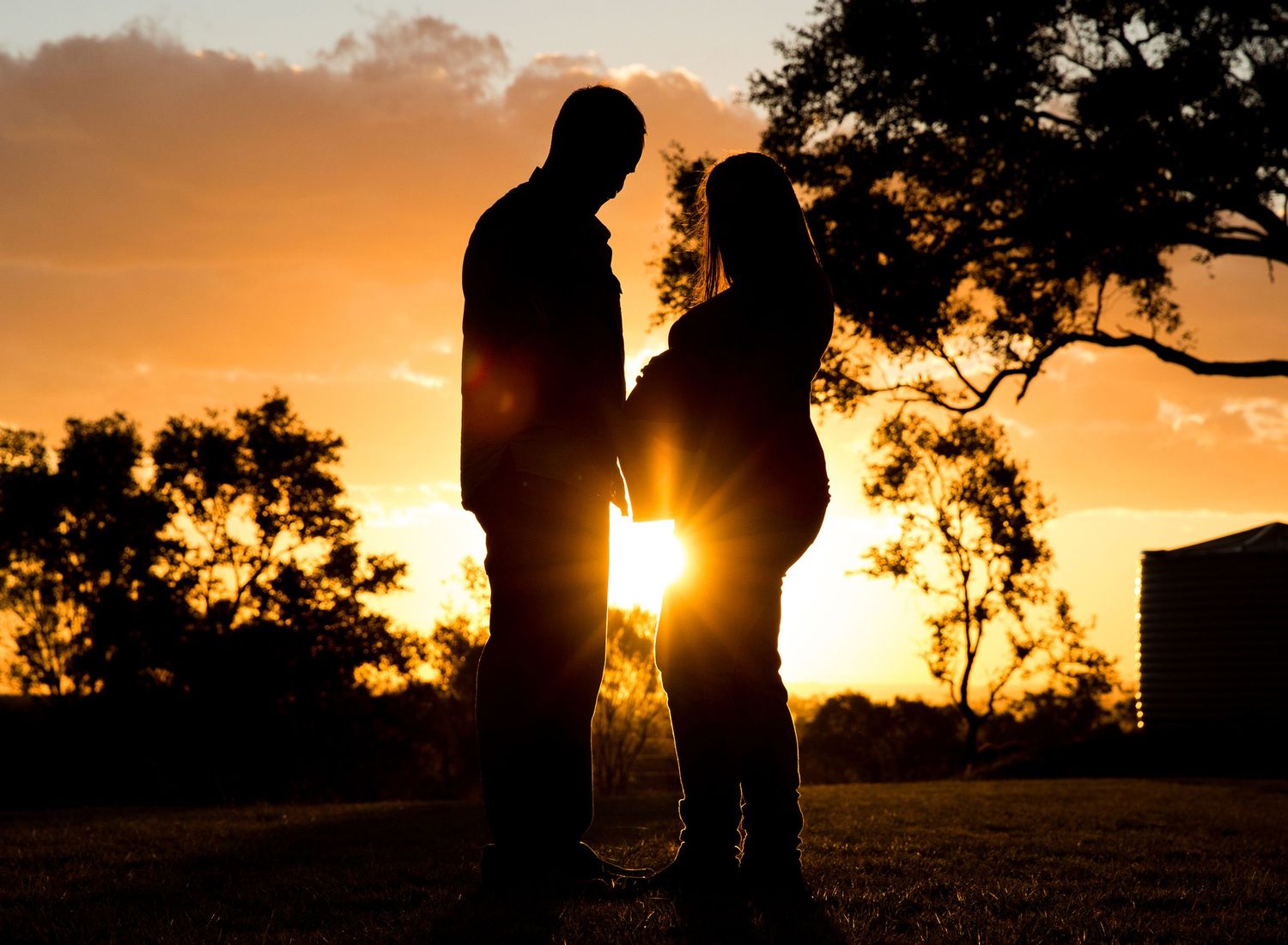 Silhouettes against a dramatic orange sunset sky with trees in the background.Toowoomba Photographer Toowoomba Newborn Photographer