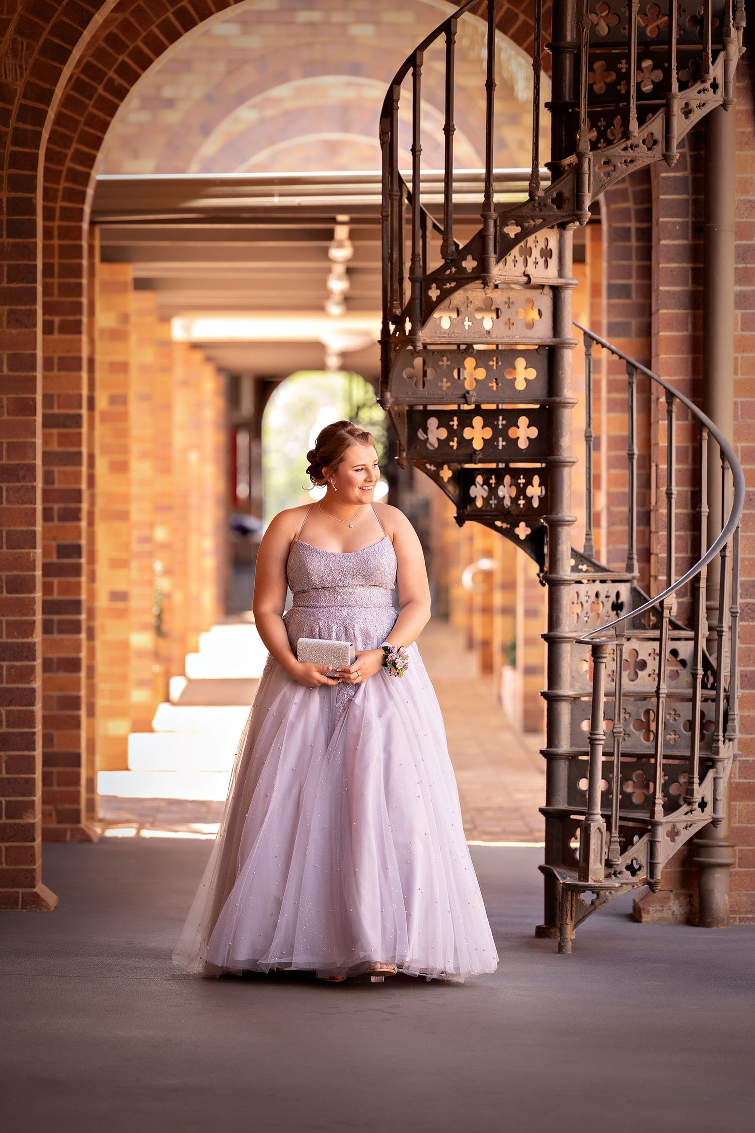 Person in lavender tulle gown poses by ornate spiral staircase in brick archway.Toowoomba Photographer Toowoomba Newborn Photographer