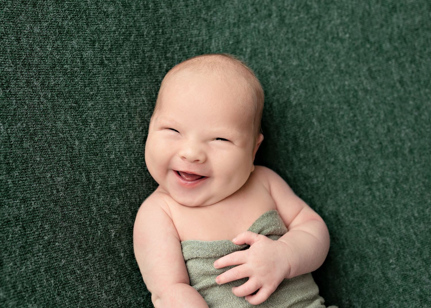 A baby in sage green clothing lies on a dark green textured backdrop in a series of photos.