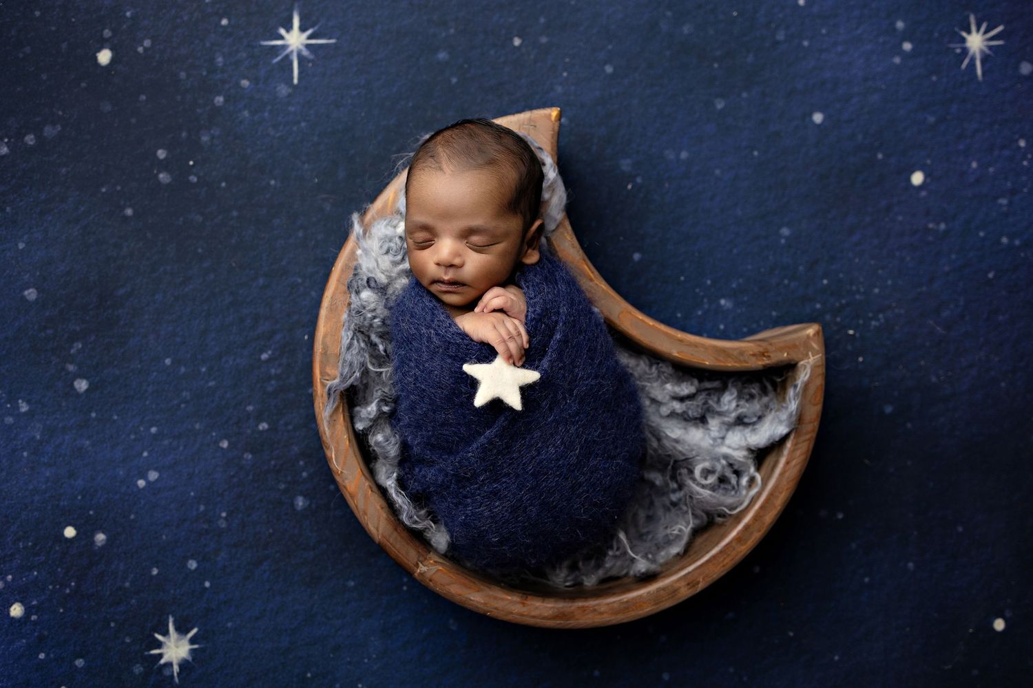 Artistic newborn portrait series with starry night sky background and wooden moon prop.
