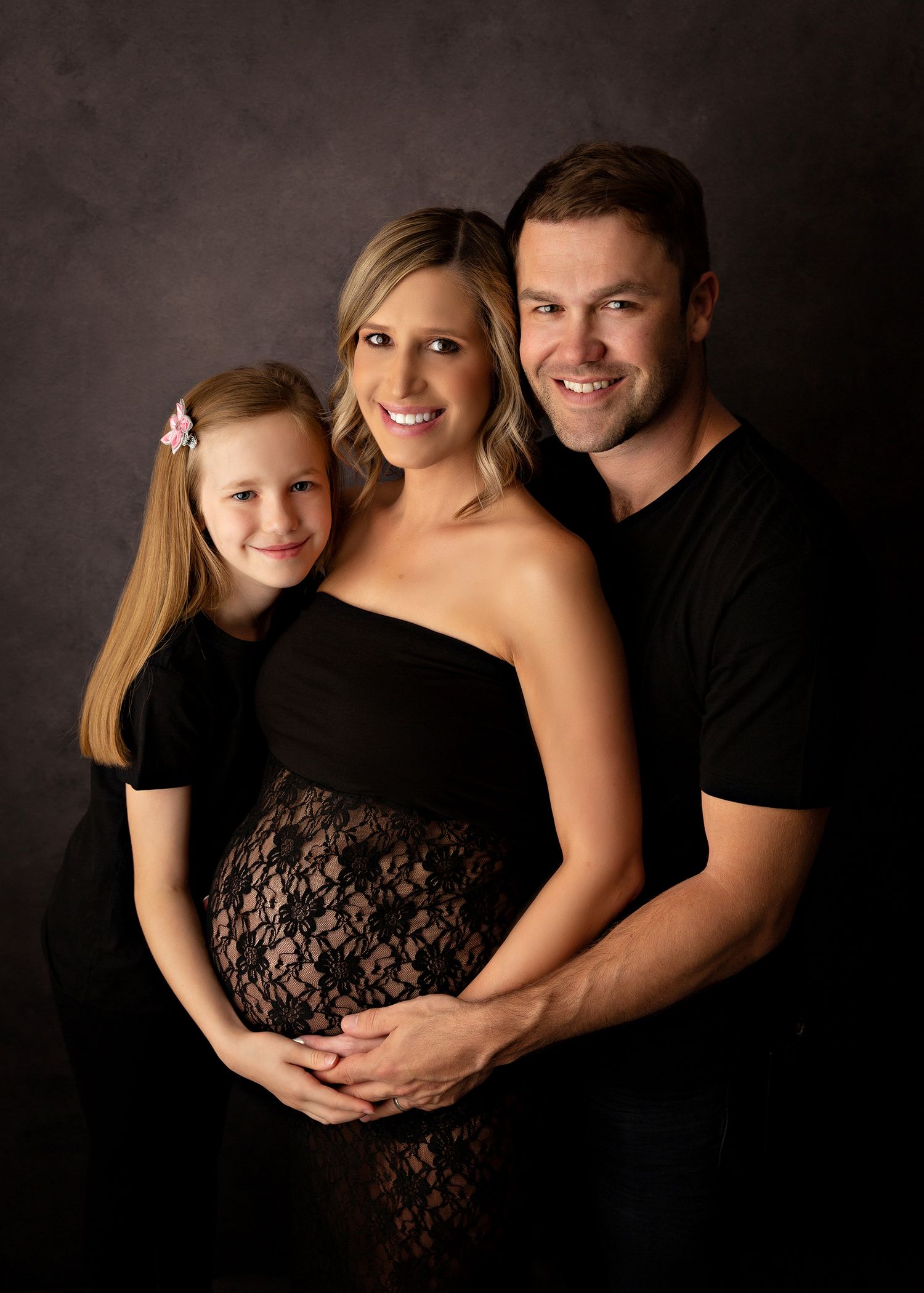 Family maternity portrait with black attire against dark studio background.