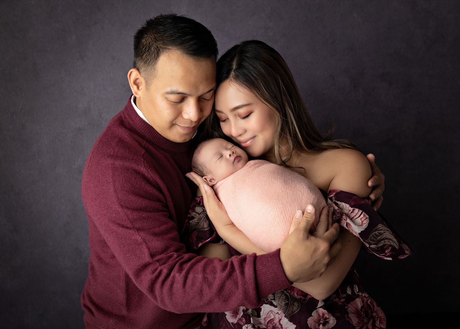 Family of three sharing intimate moment with newborn against dark background.