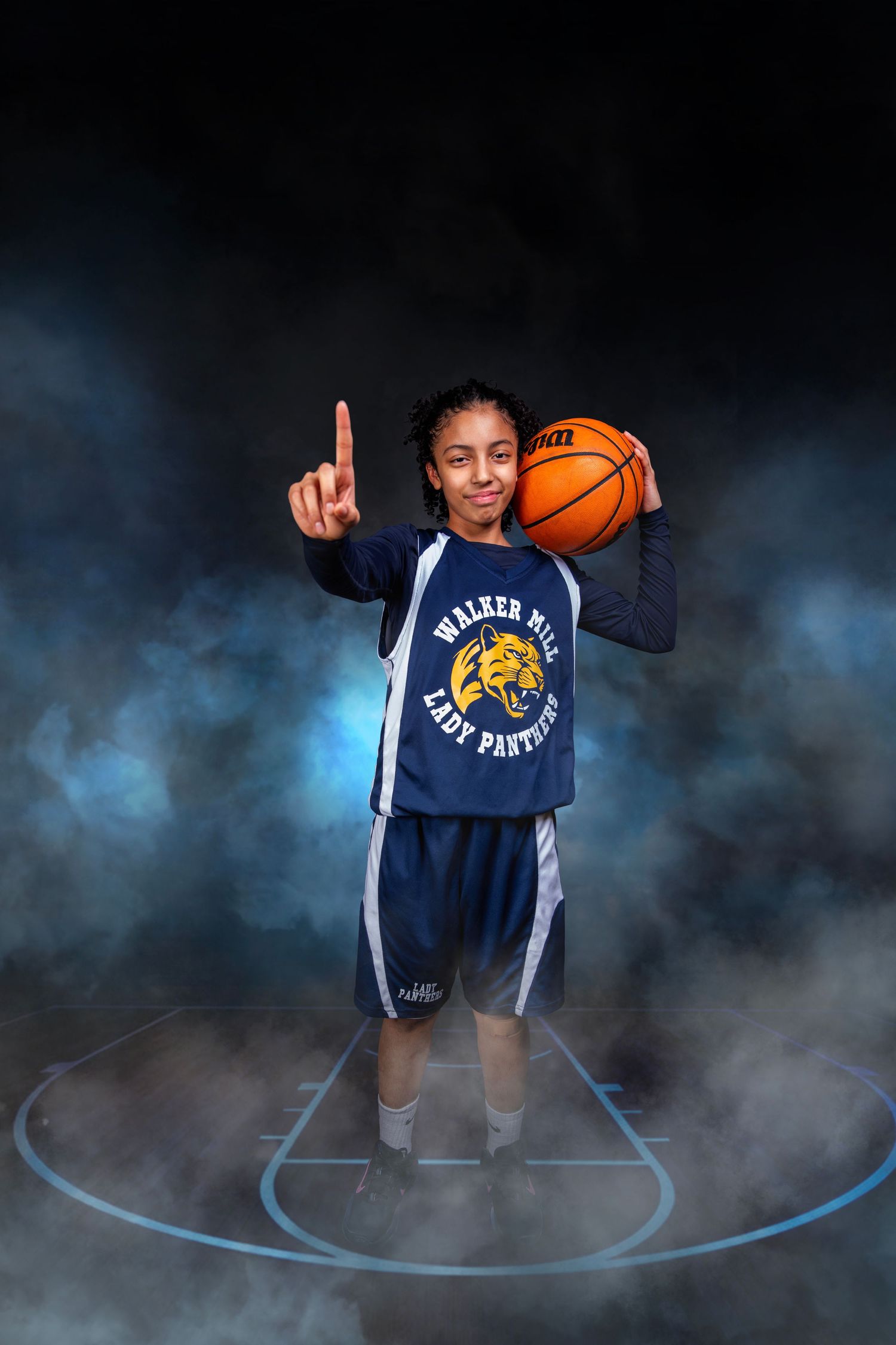 Young female basketball player in Walker Mill Lady Panthers jersey pointing upward with basketball.