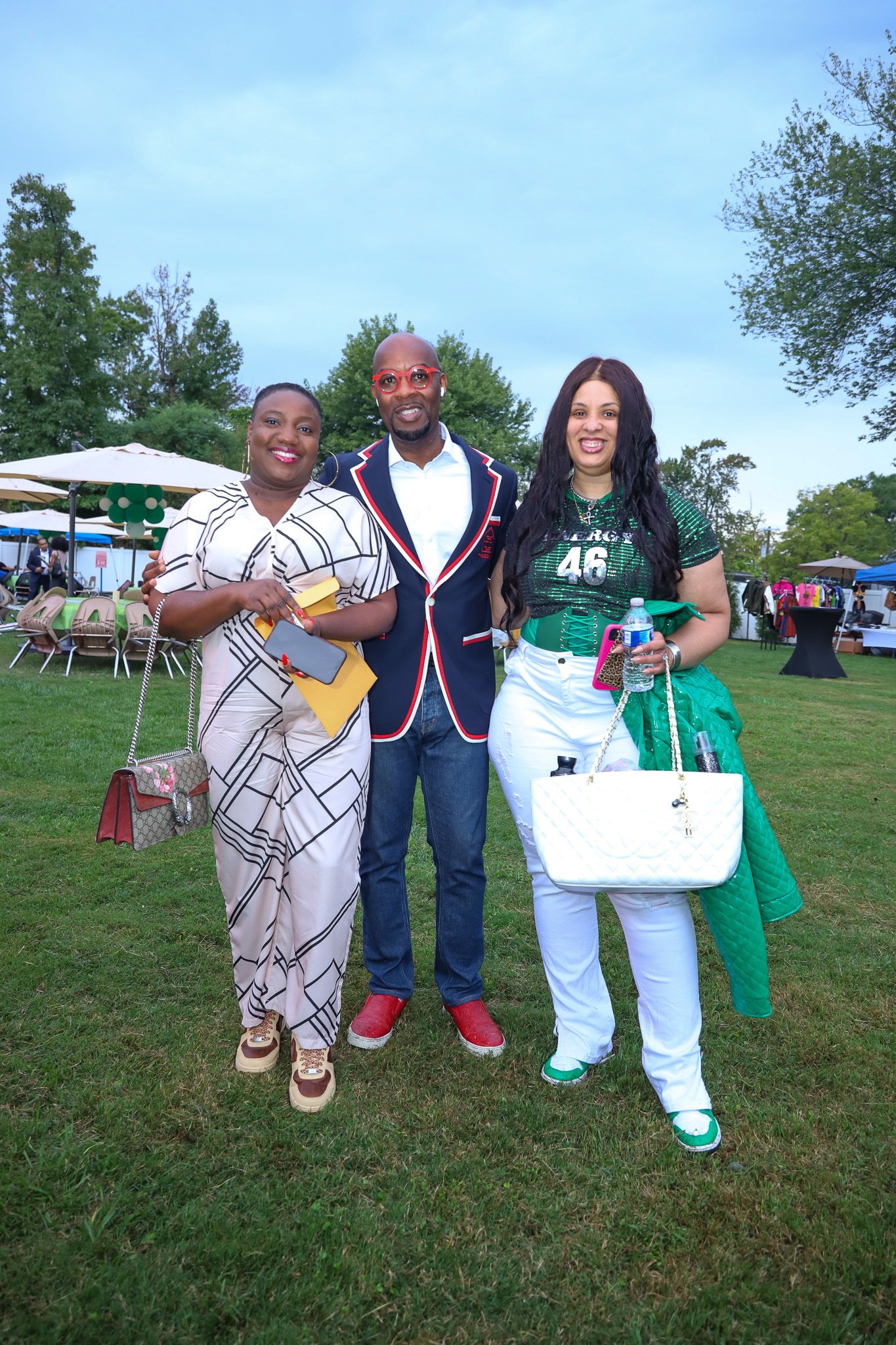 Three well-dressed African Americans posing outdoors at evening social event, man in blazer flanked by two women.