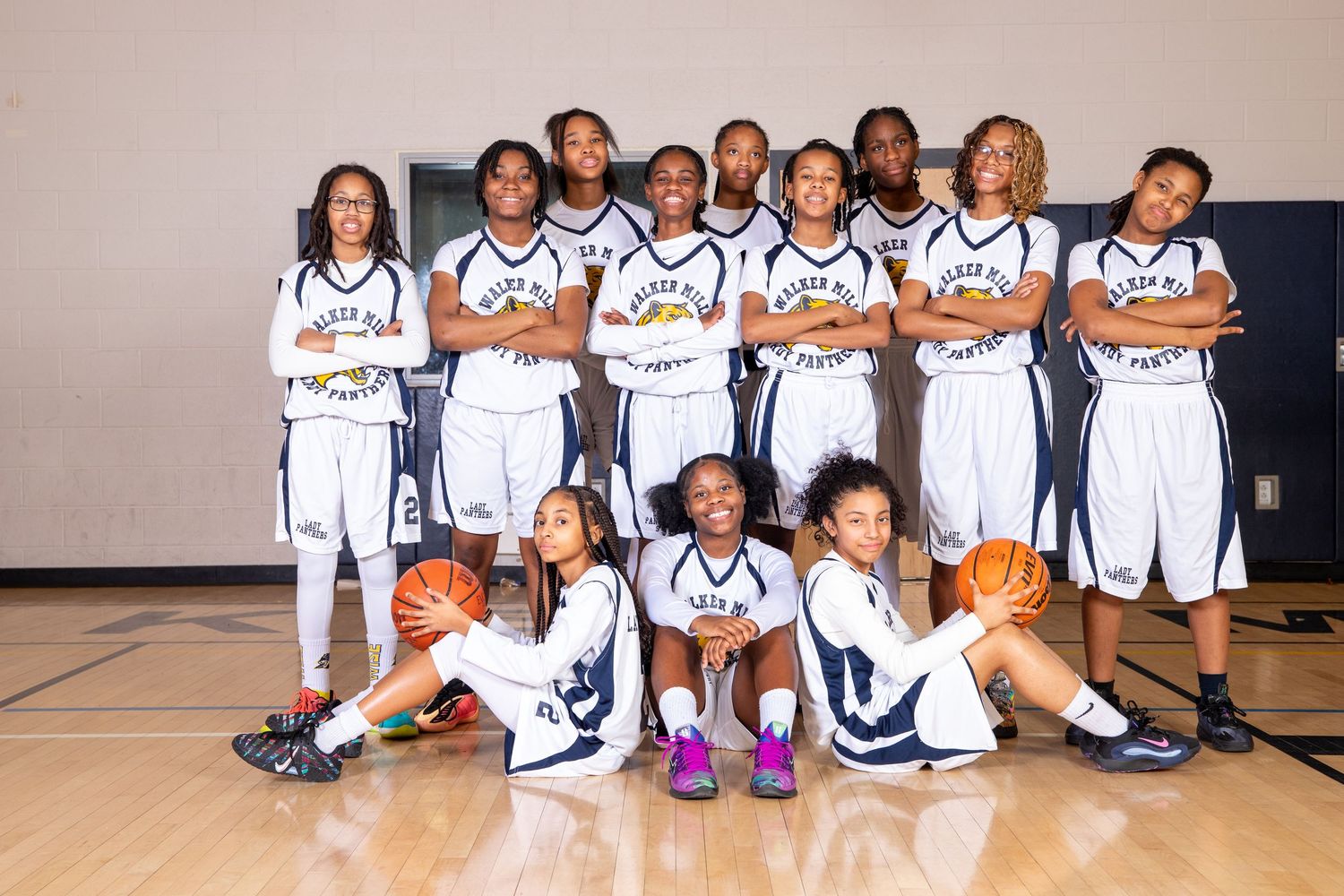 Youth basketball team members pose together in white uniforms on a gymnasium court for a team photo.