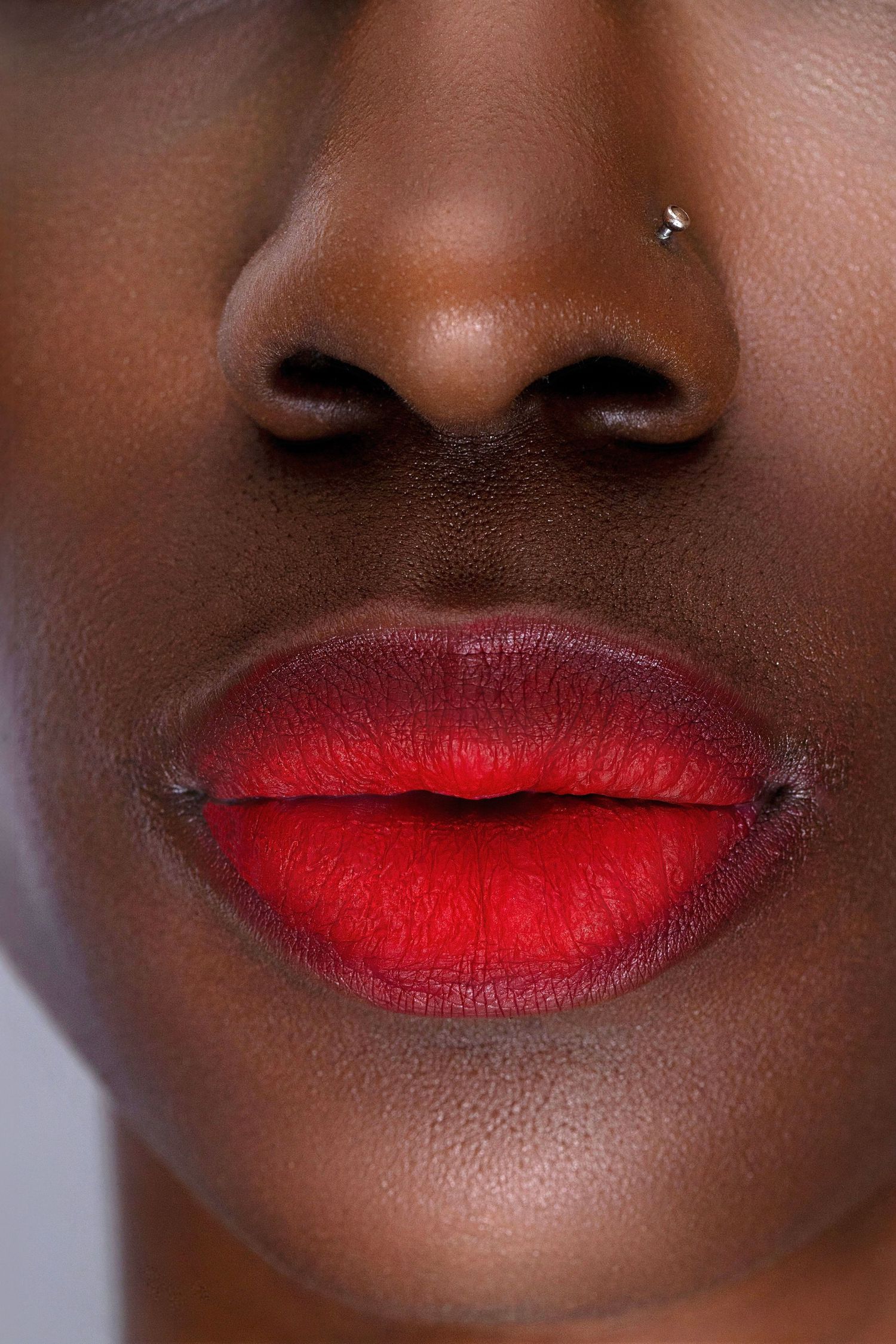 Close-up of full lips with bold red lipstick and nose piercing on dark skin.