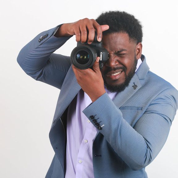 Professional male photographer in blue suit holding Canon camera against white background.