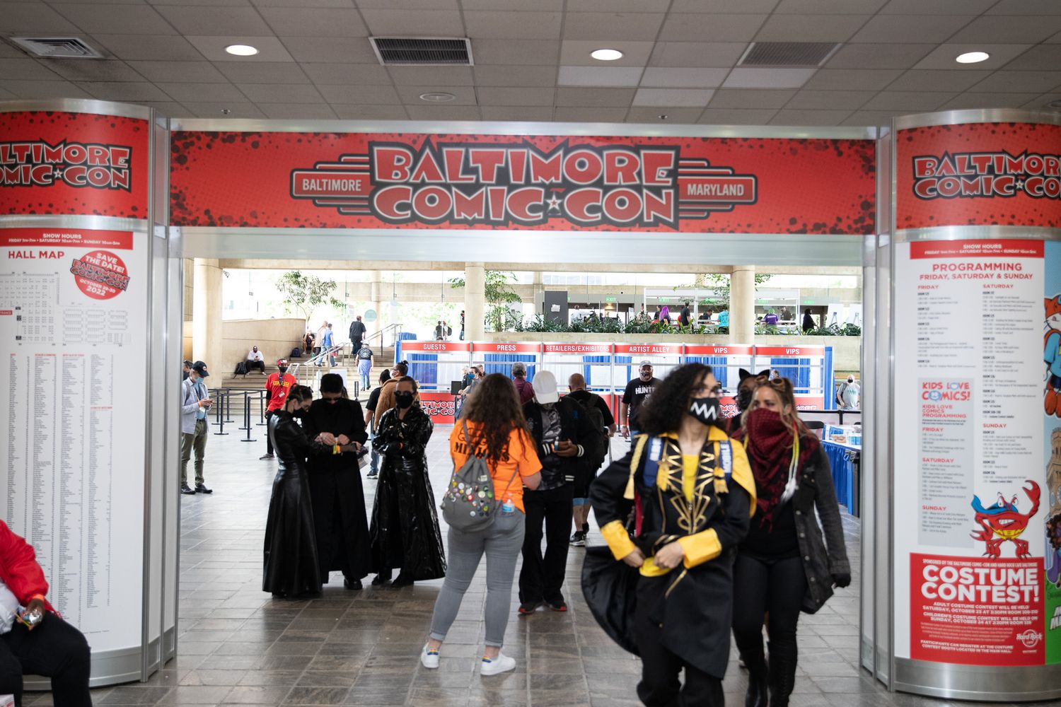 Diverse crowd of costumed attendees entering Baltimore Comic-Con through decorated entrance archway.