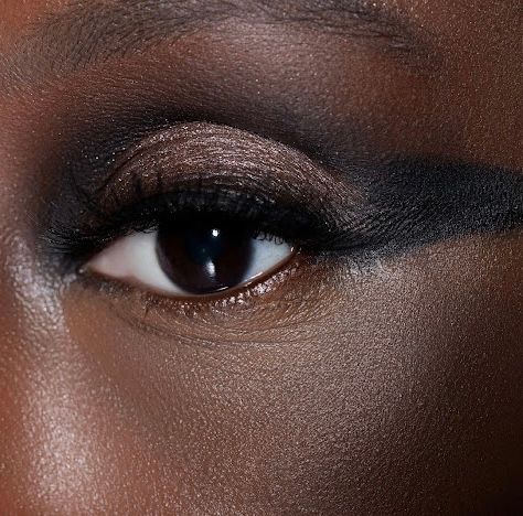 Close-up of dark skin eye with dramatic smoky bronze eyeshadow and bold black winged eyeliner makeup look.