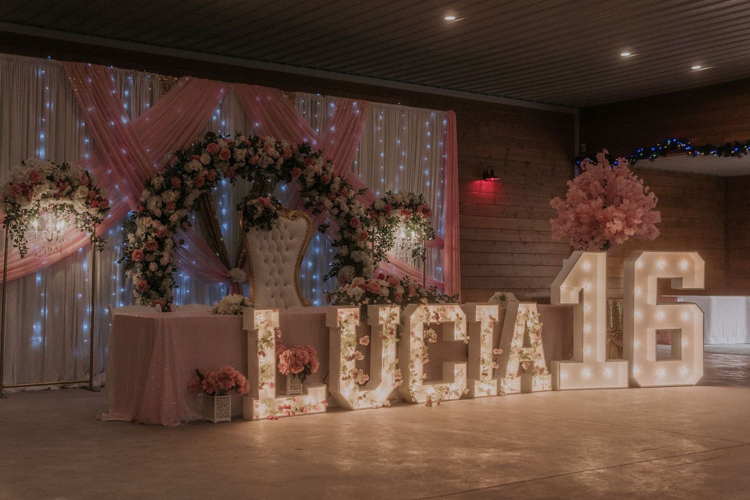 Elegant event venue decorated with pink floral arrangements and illuminated letter signage.