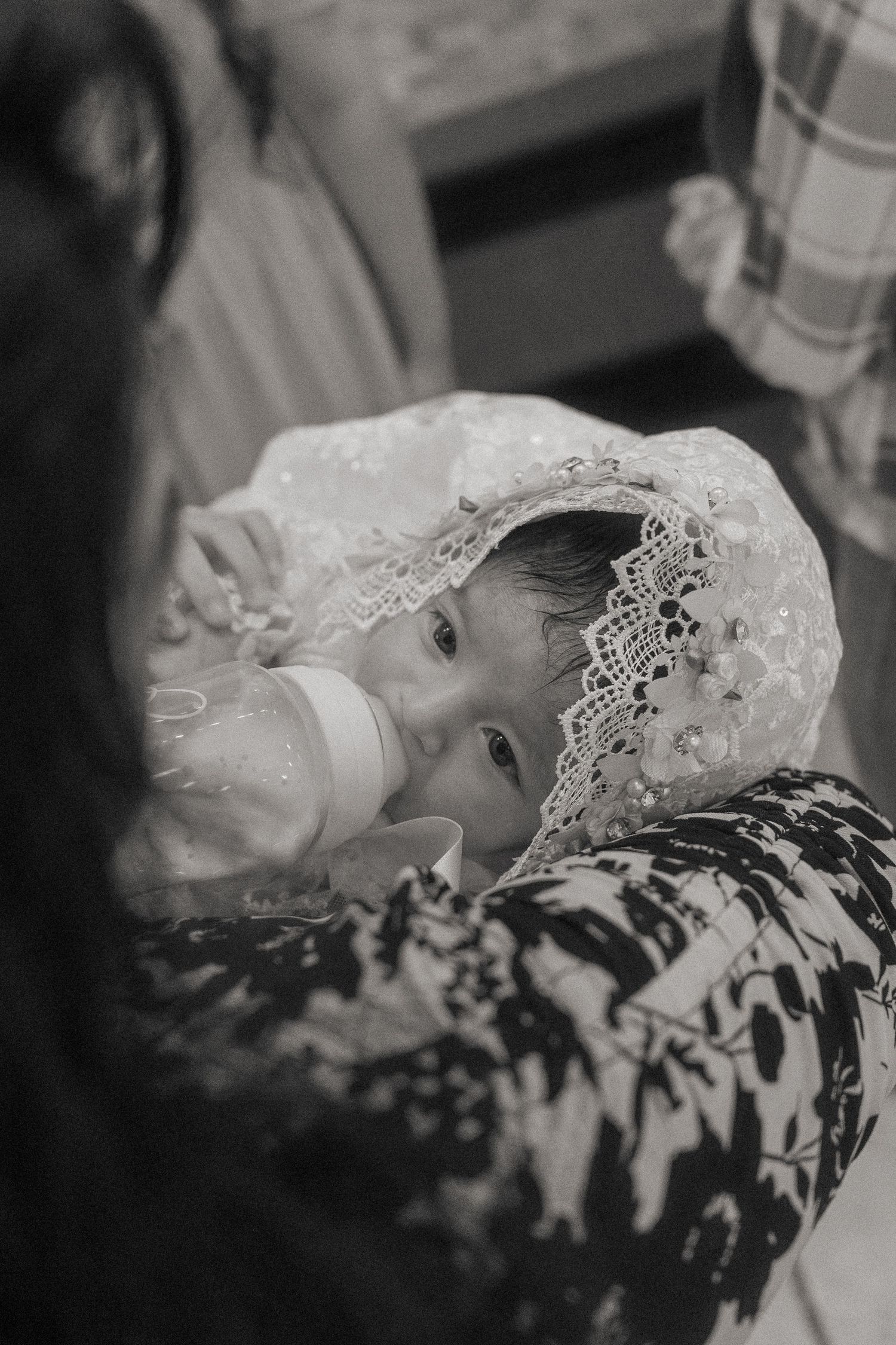 Baby in white lace christening gown resting on floral fabric.