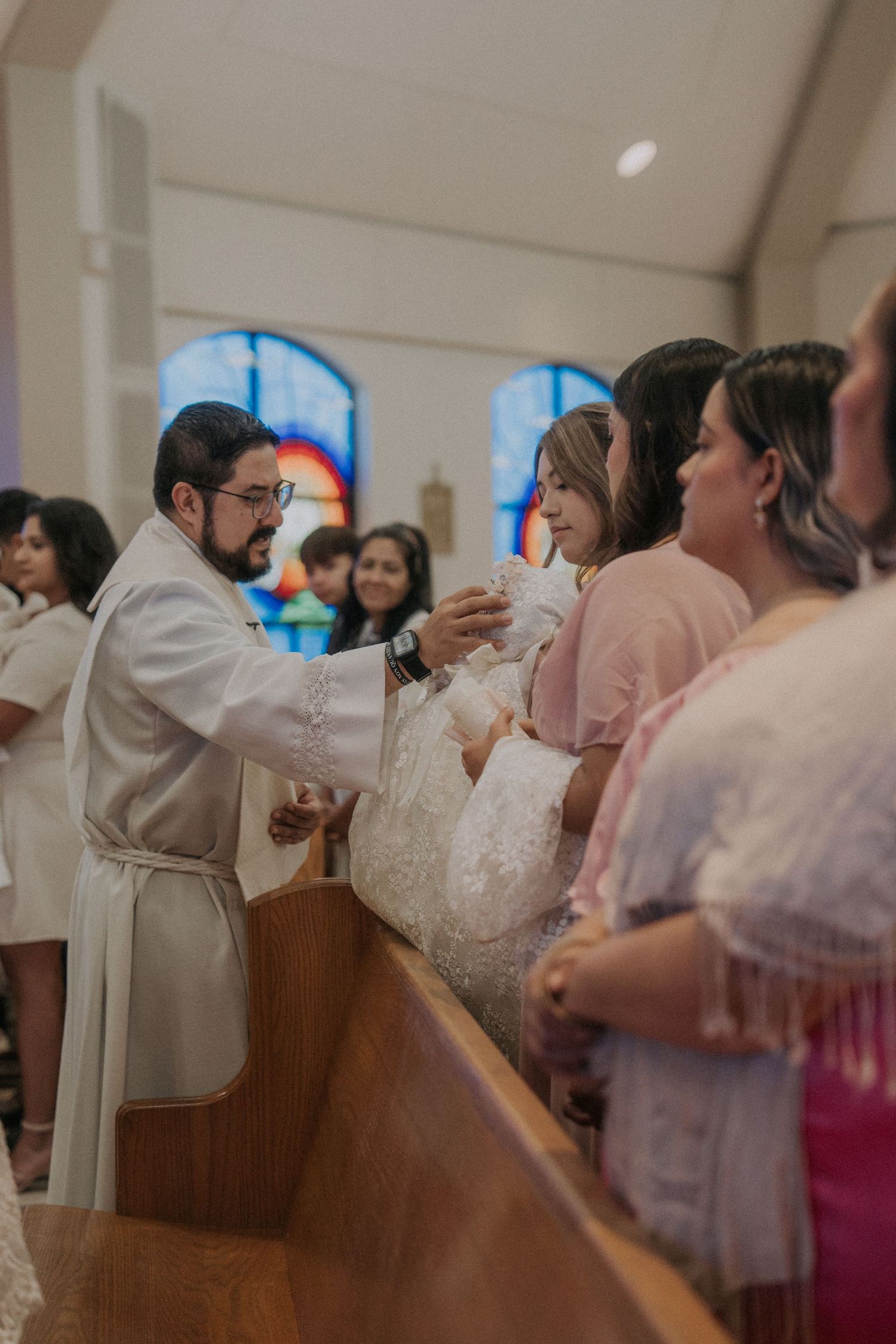 Church congregation gathered in wooden pews during a baptism ceremony with pink and white decor.