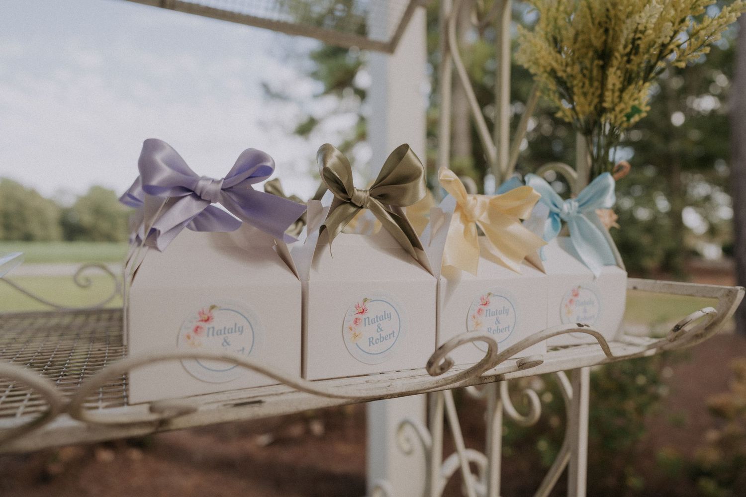 Three white gift boxes with colorful ribbon bows displayed on a decorative metal shelf outdoors.