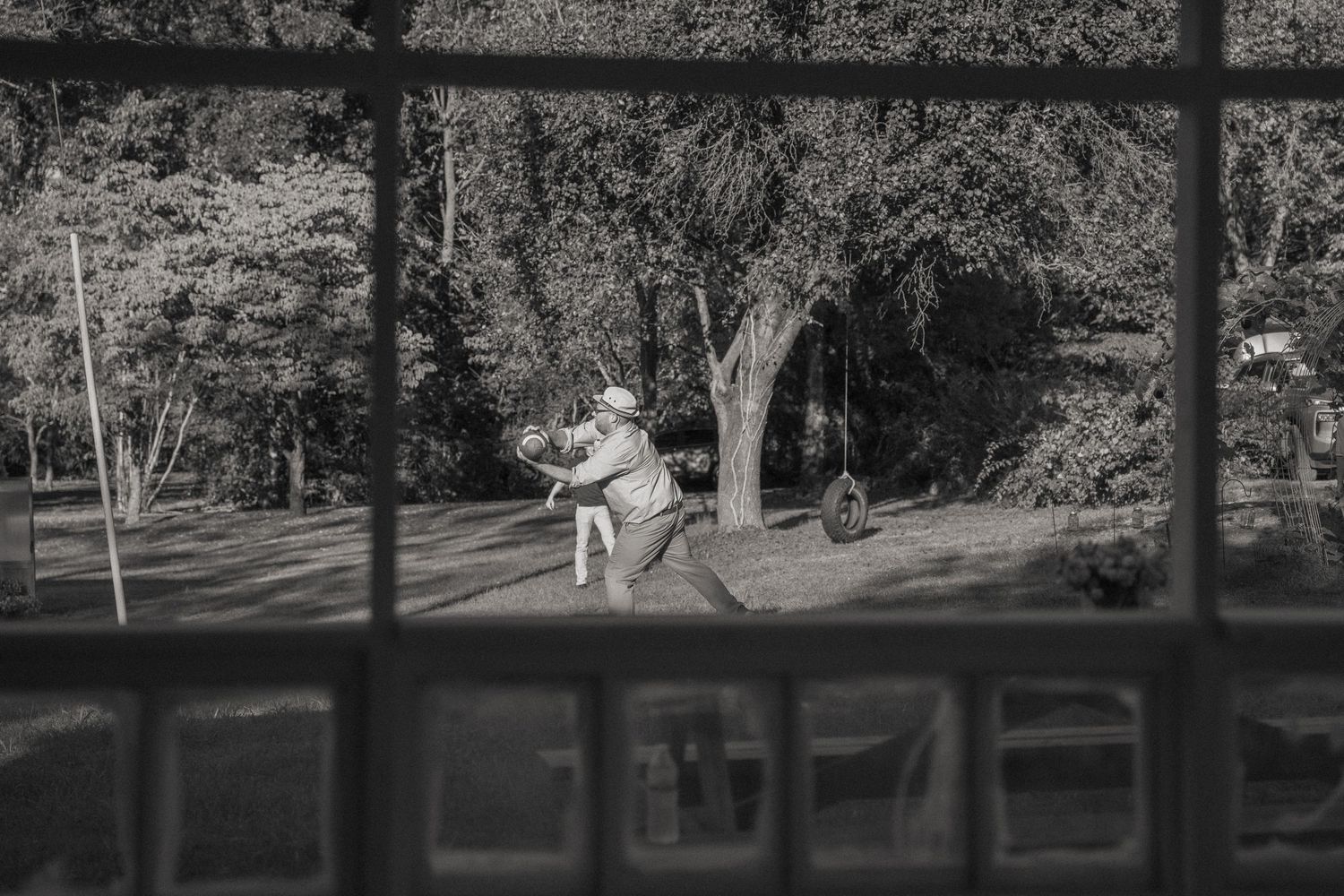 Black and white photograph of people playing in a front yard with trees casting shadows.