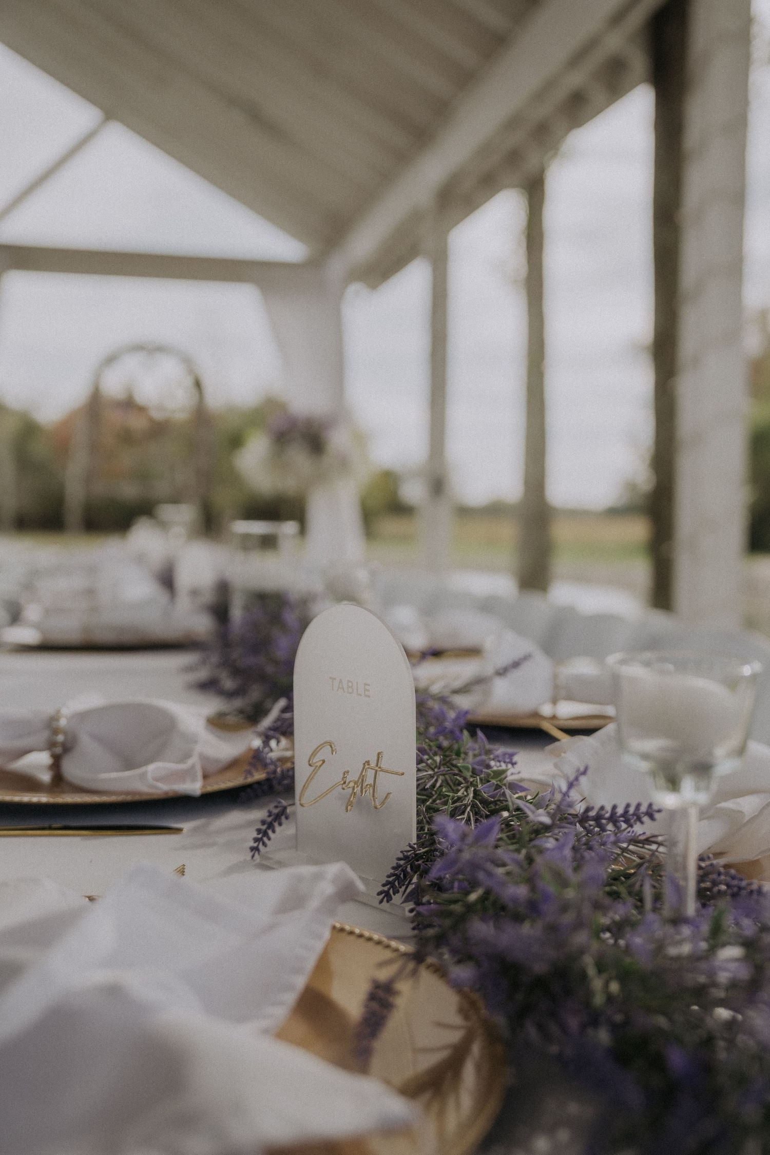 Elegant wedding table setting with purple flowers and place cards under a white tent.