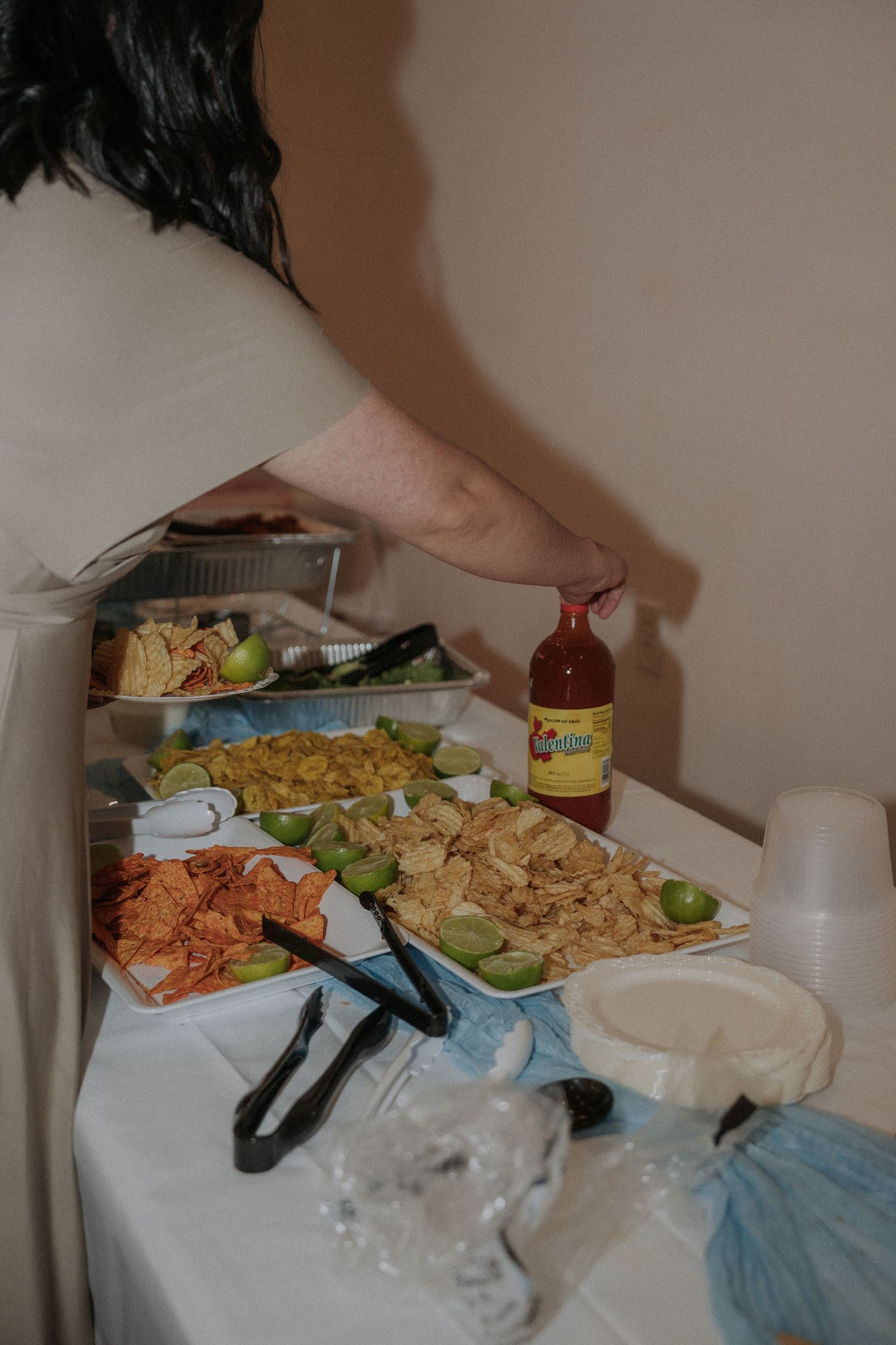 A buffet table with chips, limes, and hot sauce at a party, with a person serving food.
