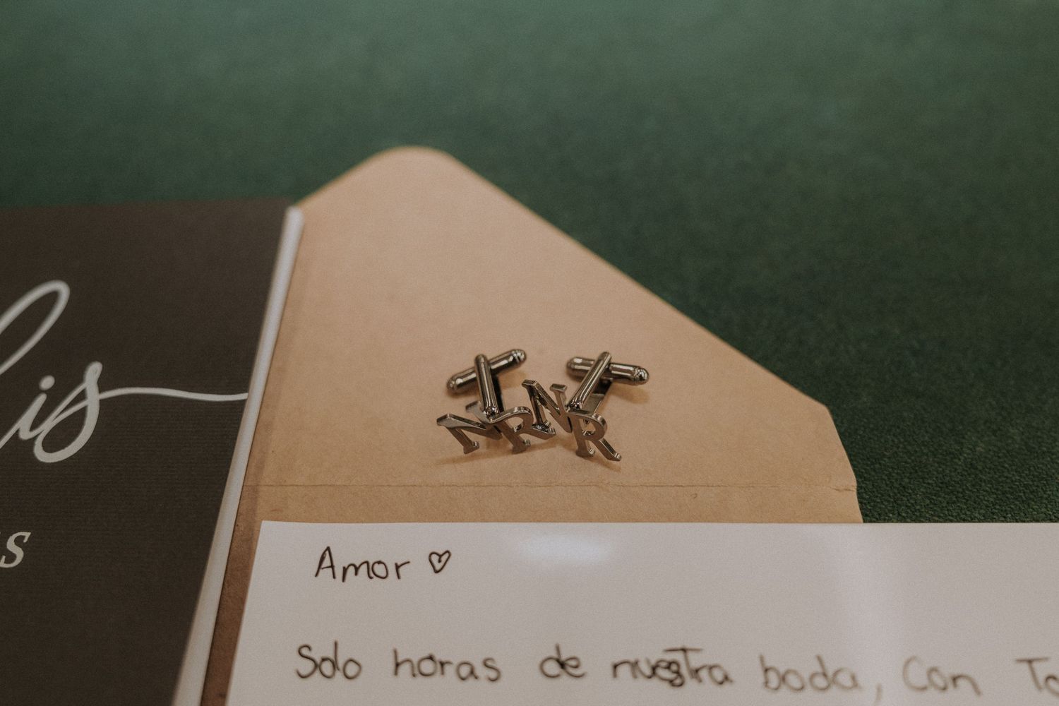 Cross cufflinks resting on a handwritten Spanish love letter in an envelope on a green surface.
