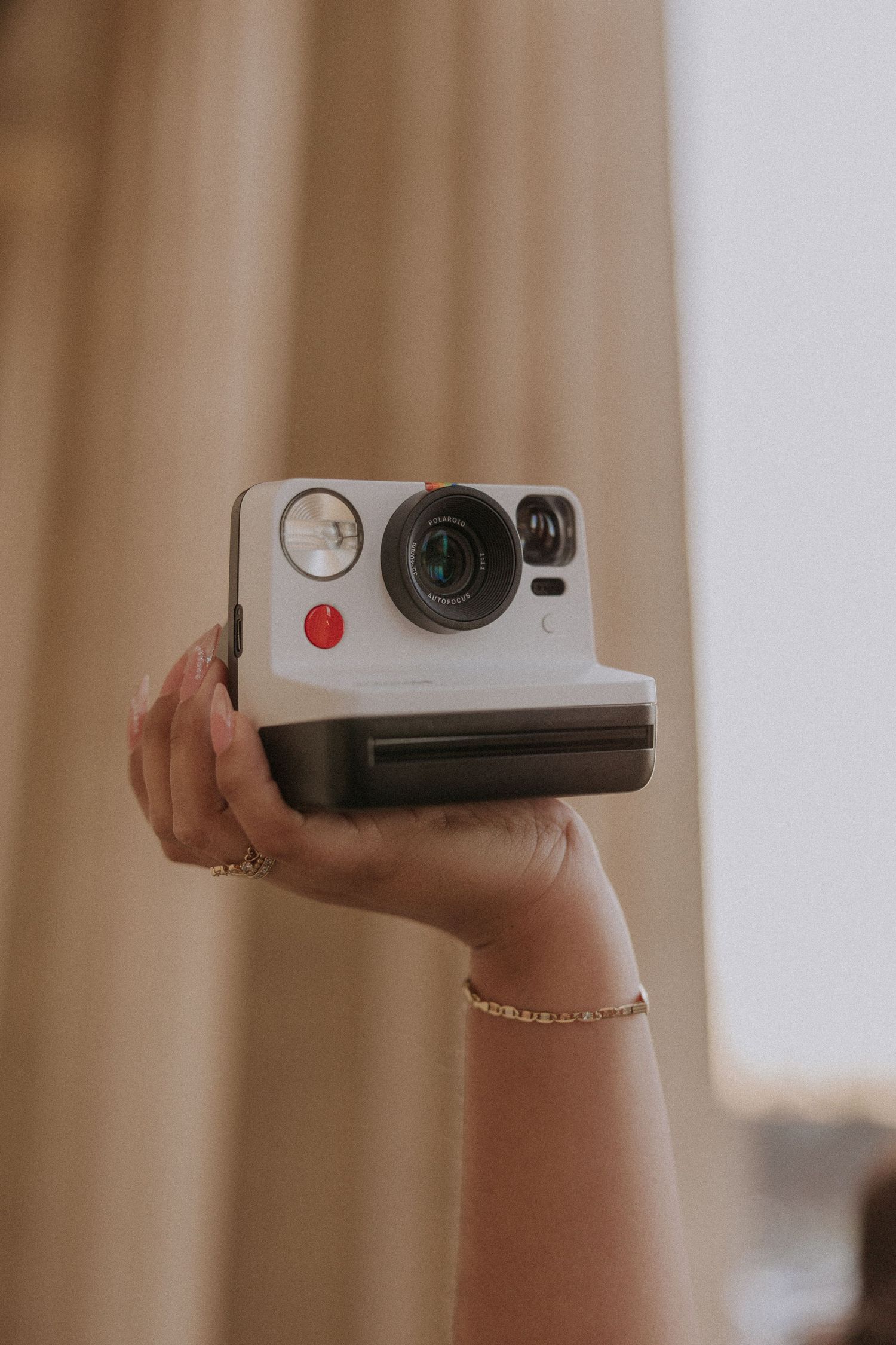 Hand holding a vintage-style camera against a soft beige background.