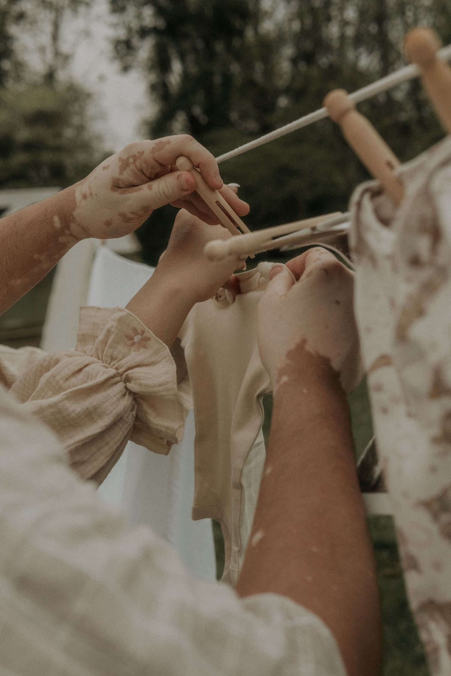 Close-up of hands holding a newborn outfit against a soft, dreamy, clothesline background