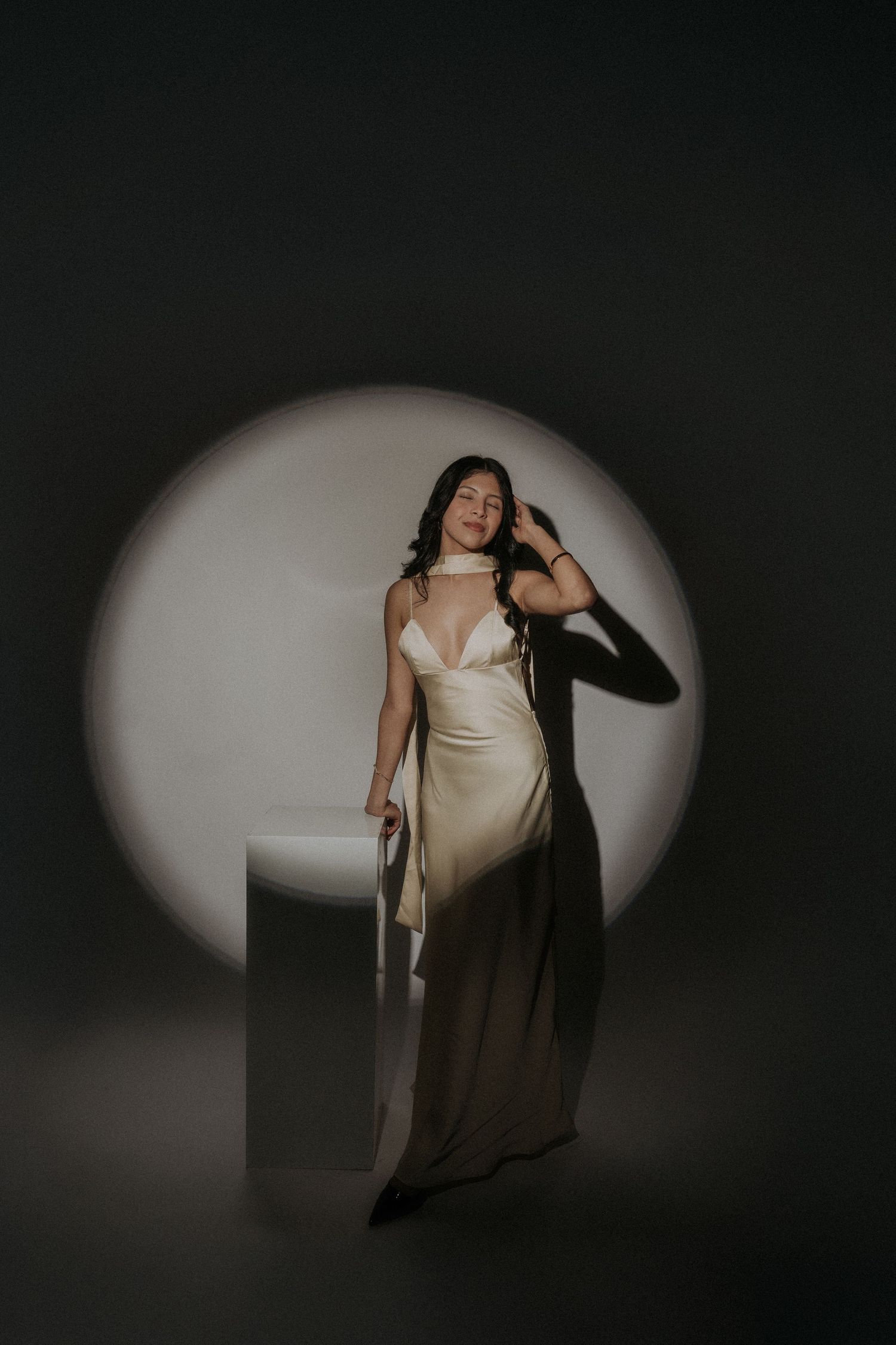 Artistic portrait in a pastel yellow dress against dramatic spotlight lighting and dark background.