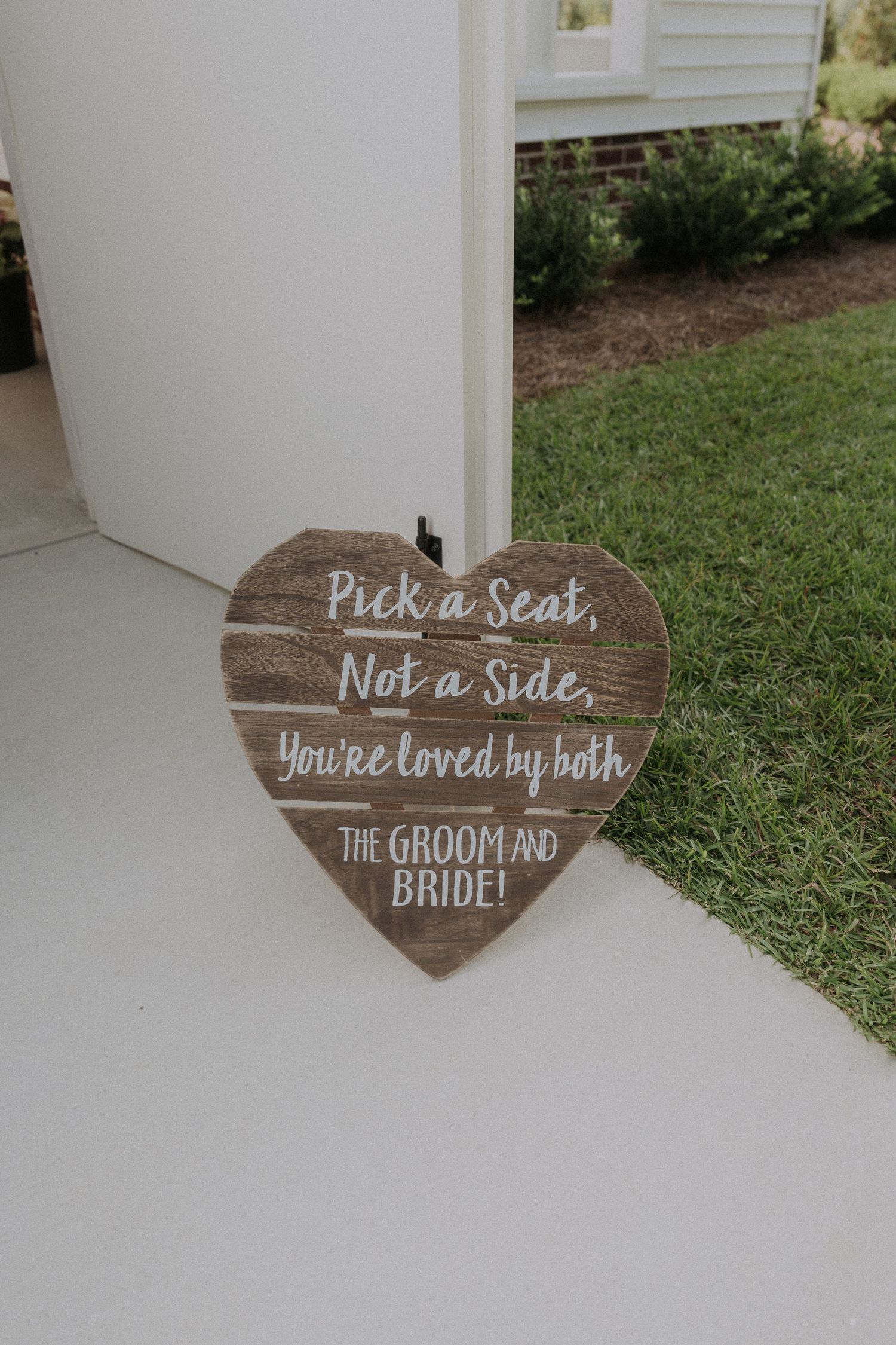 Rustic heart-shaped wooden wedding sign reading Pick a Seat Not a Side You're Loved by Both.