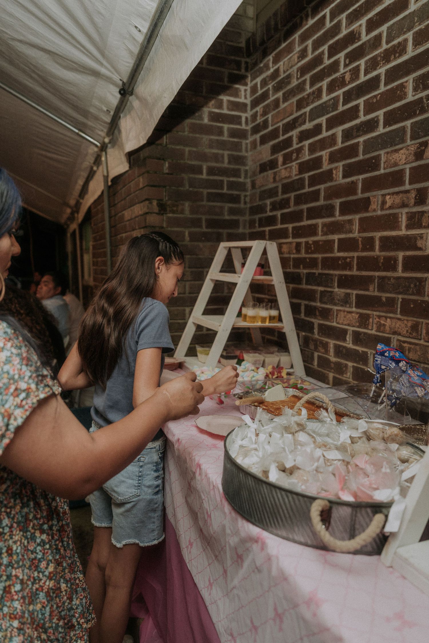 Dessert table setup against brick wall with pink decor and white linens.
