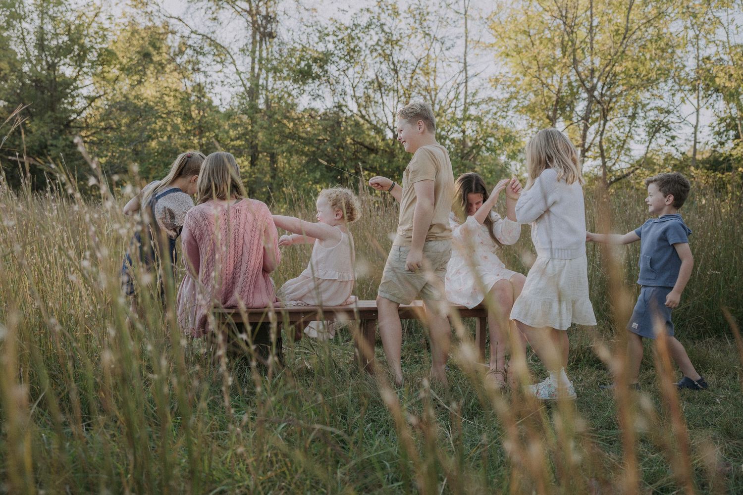 Group of people playing and running through a sunlit meadow with trees in the background.