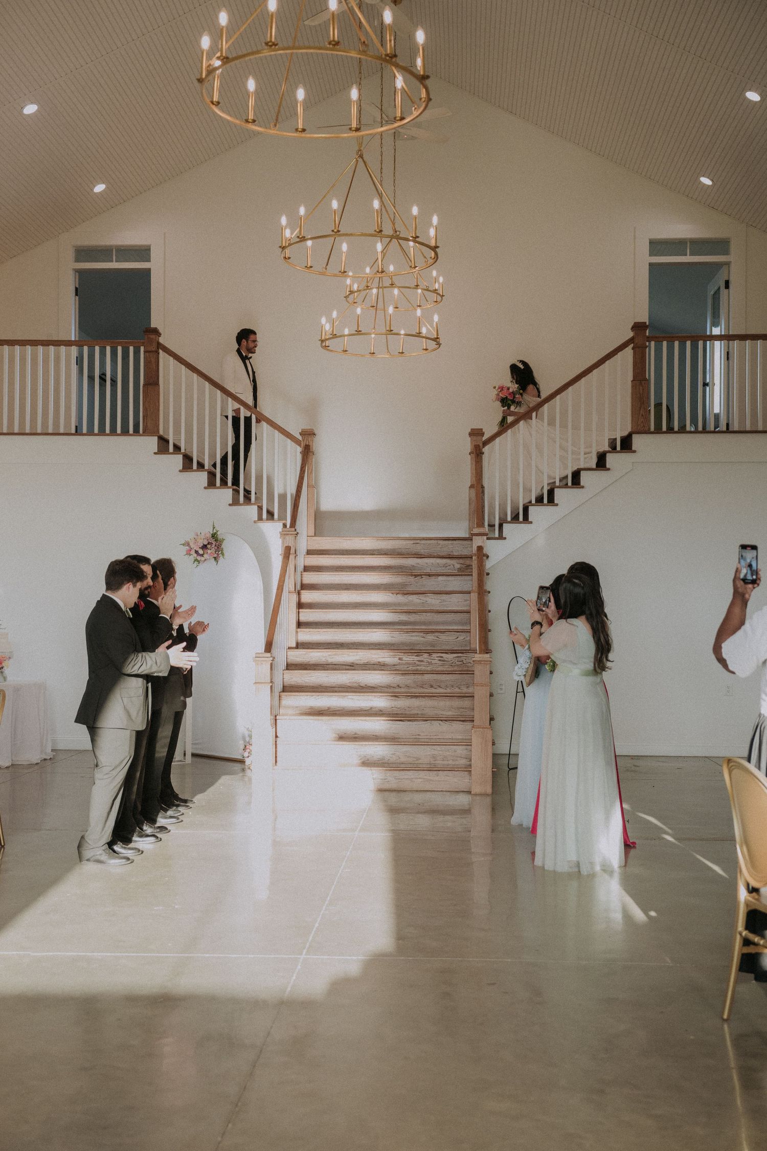 Elegant wedding venue with grand dual staircases, gold chandelier, and guests gathered for a ceremony celebration.