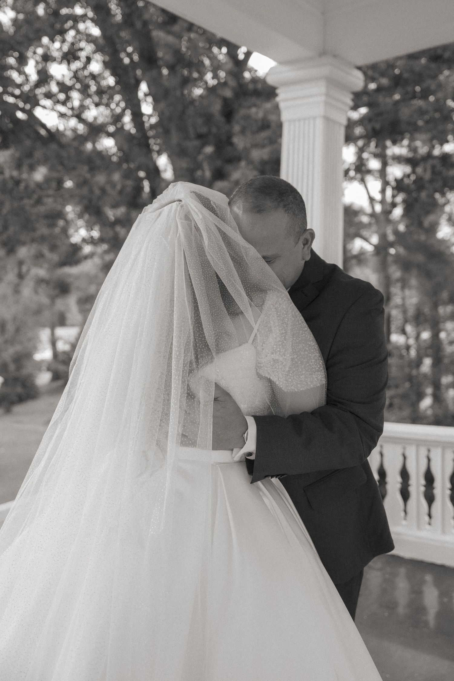 Black and white photo of bride and groom sharing a kiss on a classic white columned porch.