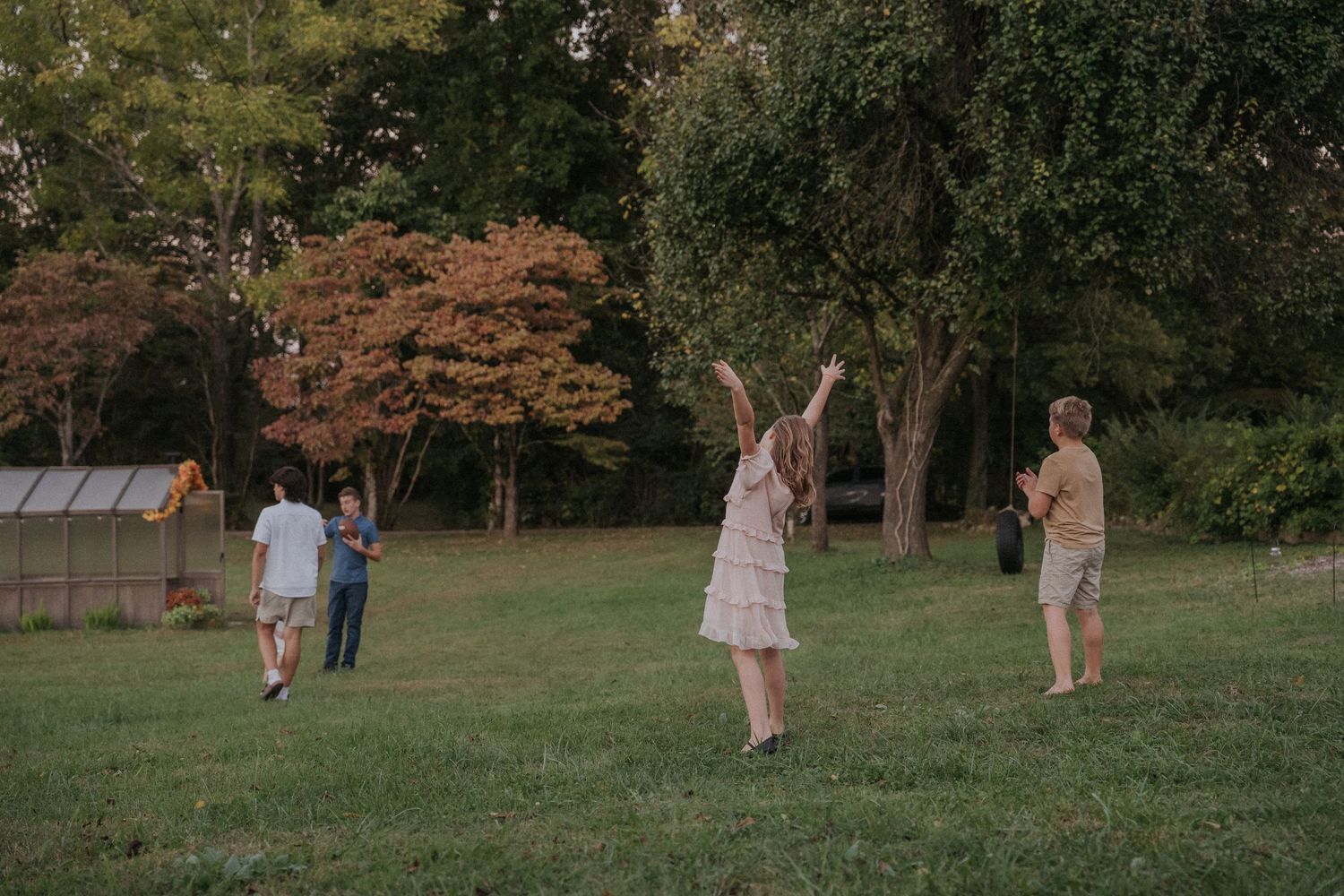 Children playing across a grassy field during golden hour with trees in background.