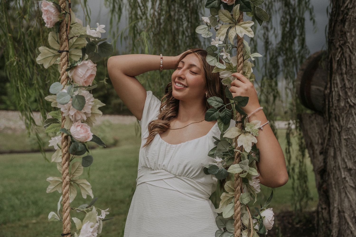 Playful poses by a decorative floral swing with willow trees in the background.