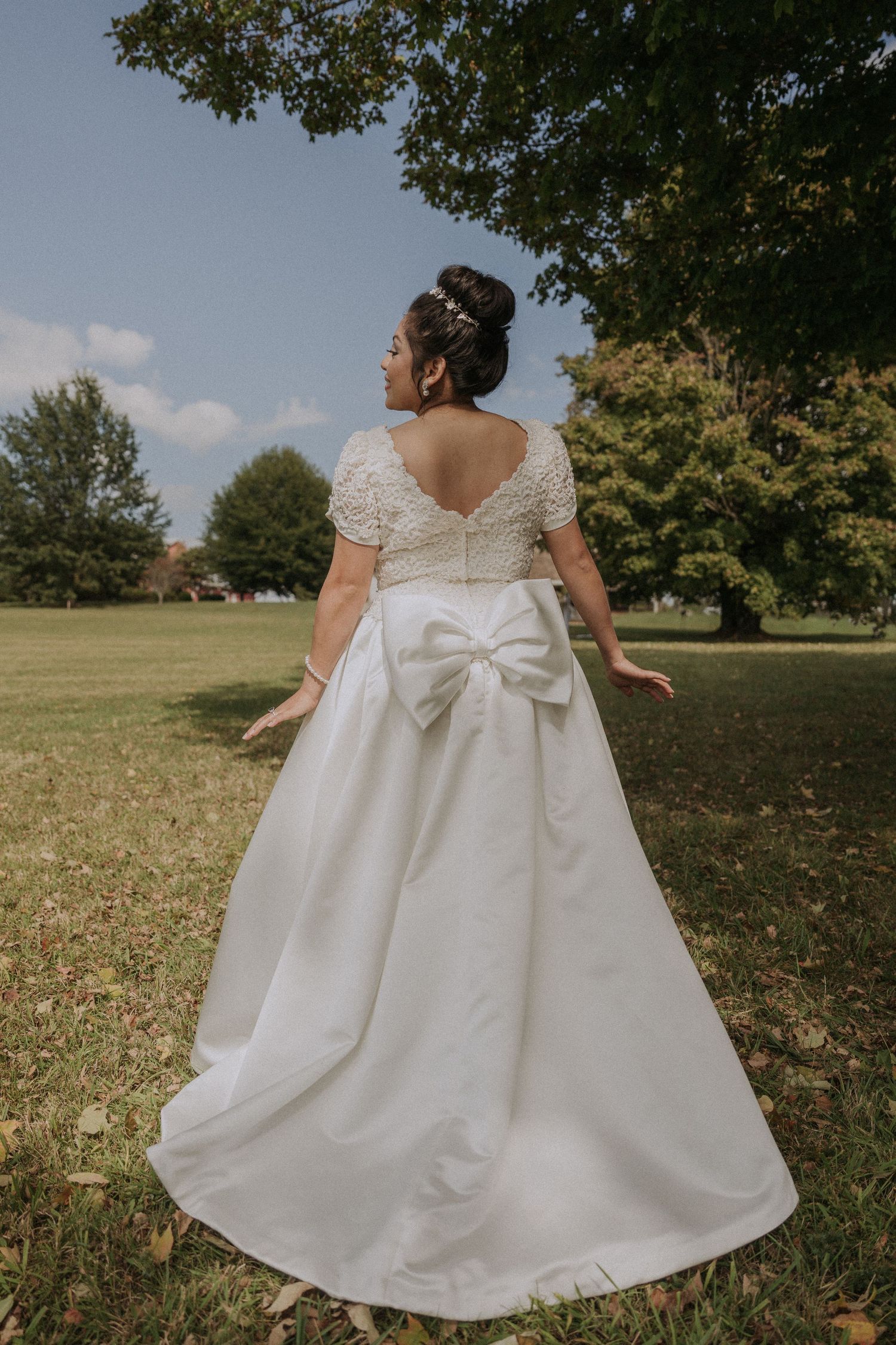 White wedding dress with lace details and large bow photographed outdoors.