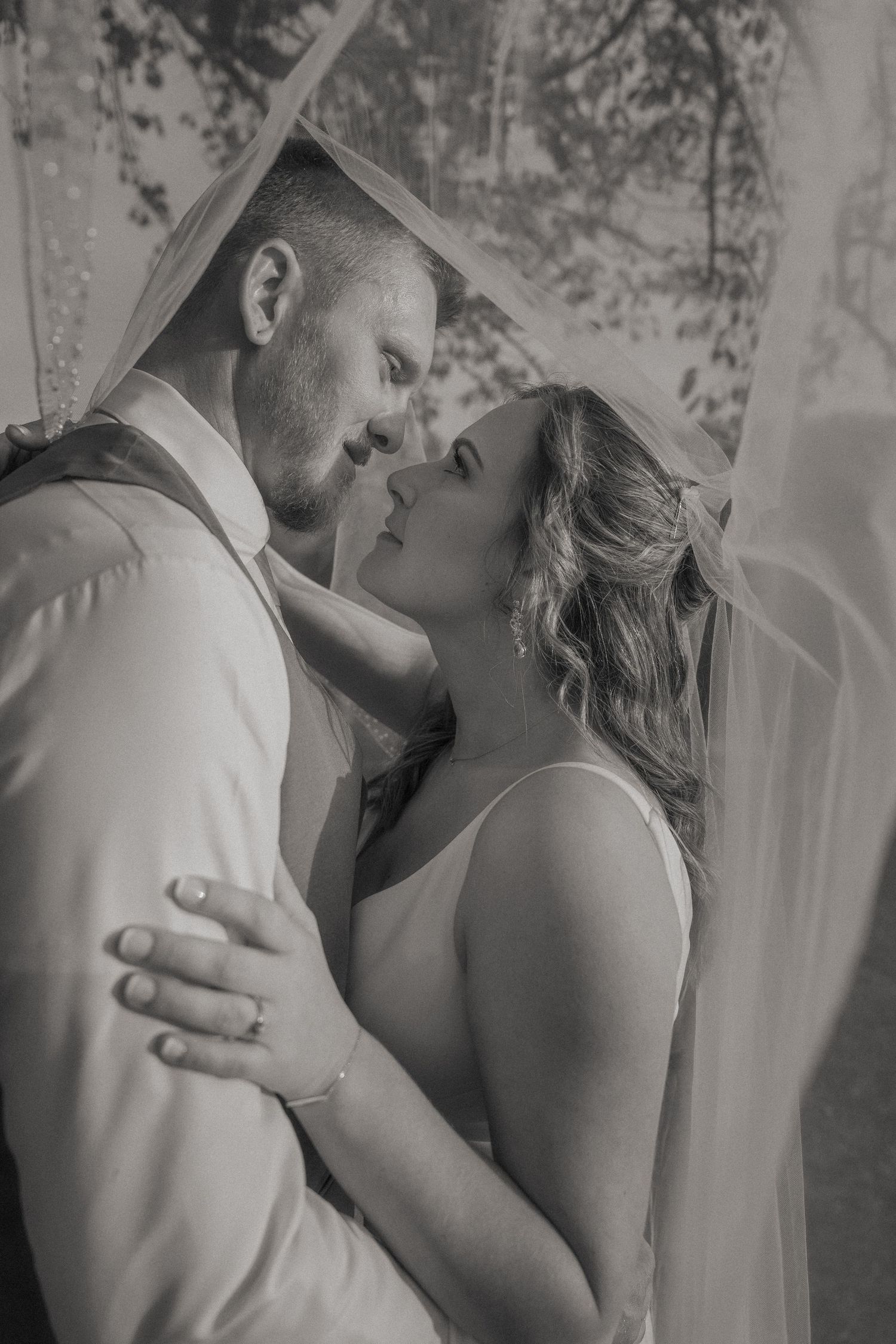 A romantic black and white wedding portrait showing a tender moment between newlyweds under a veil.