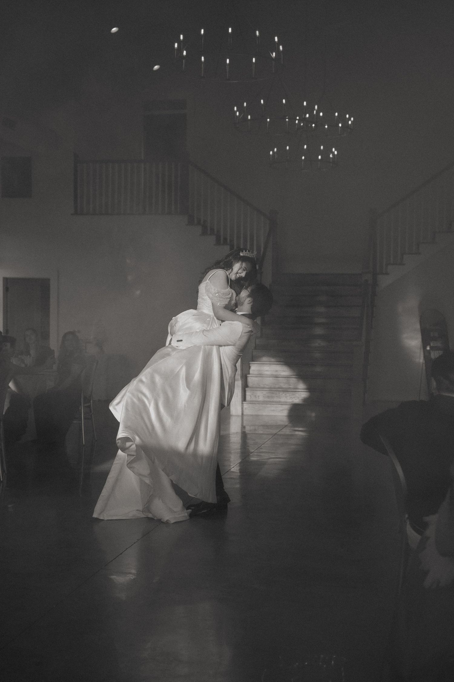Black and white photo of a groom lifting his bride during their first dance at a wedding reception.