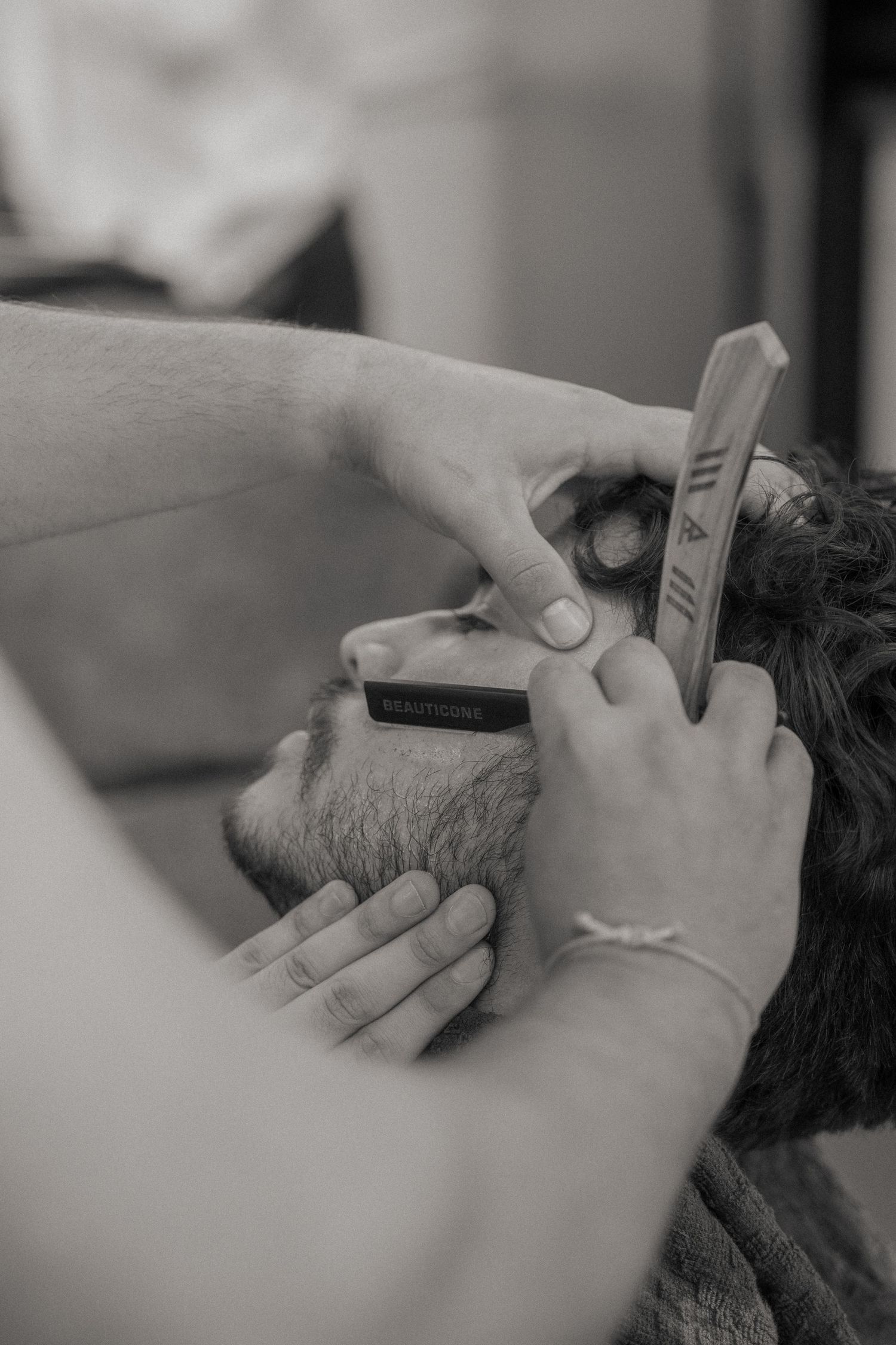 Barber using straight razor and comb to trim beard of male client in black and white photo.