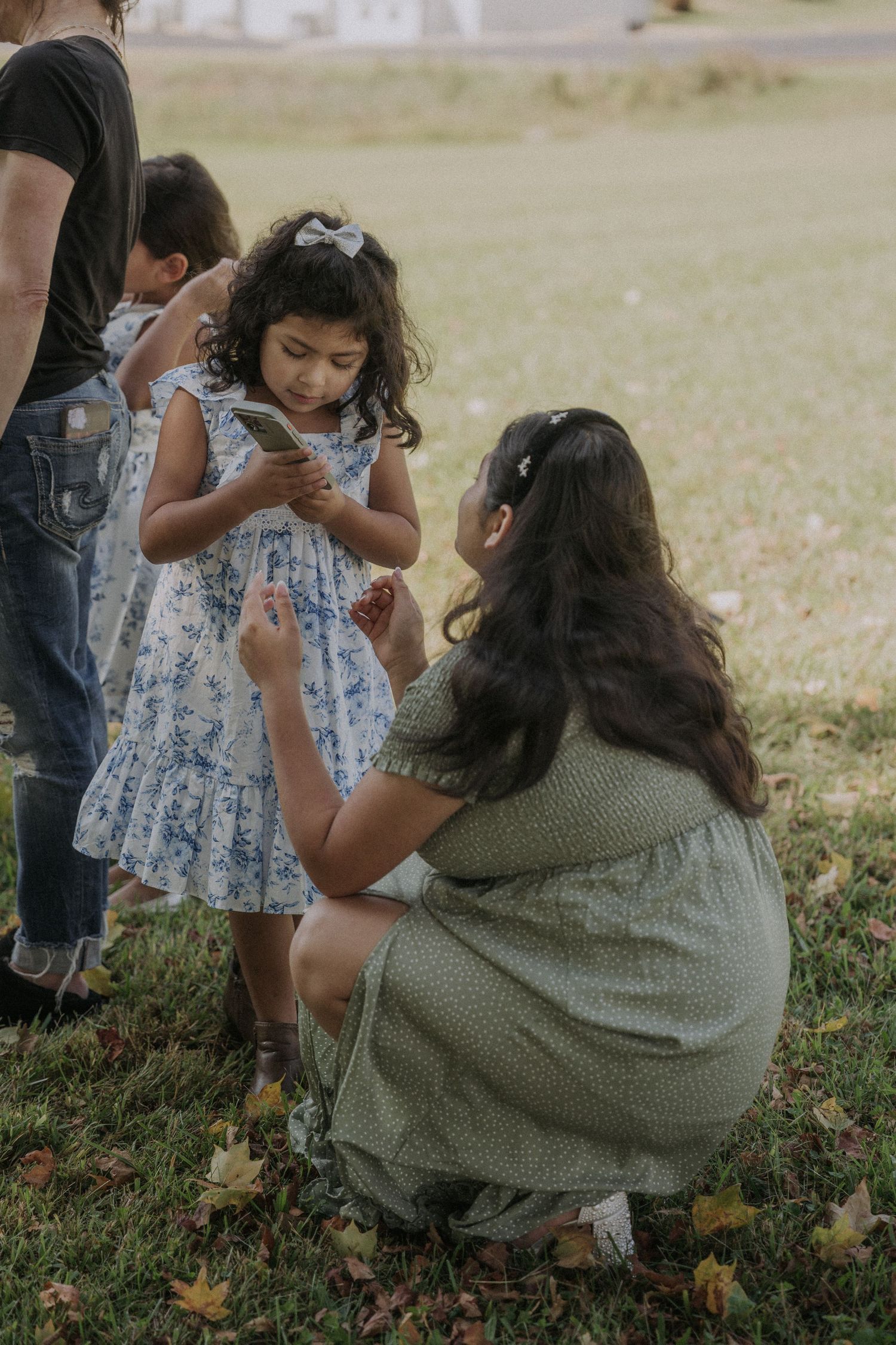 Young girls in blue floral dresses playing on autumn grass during a vow renewal ceremony.