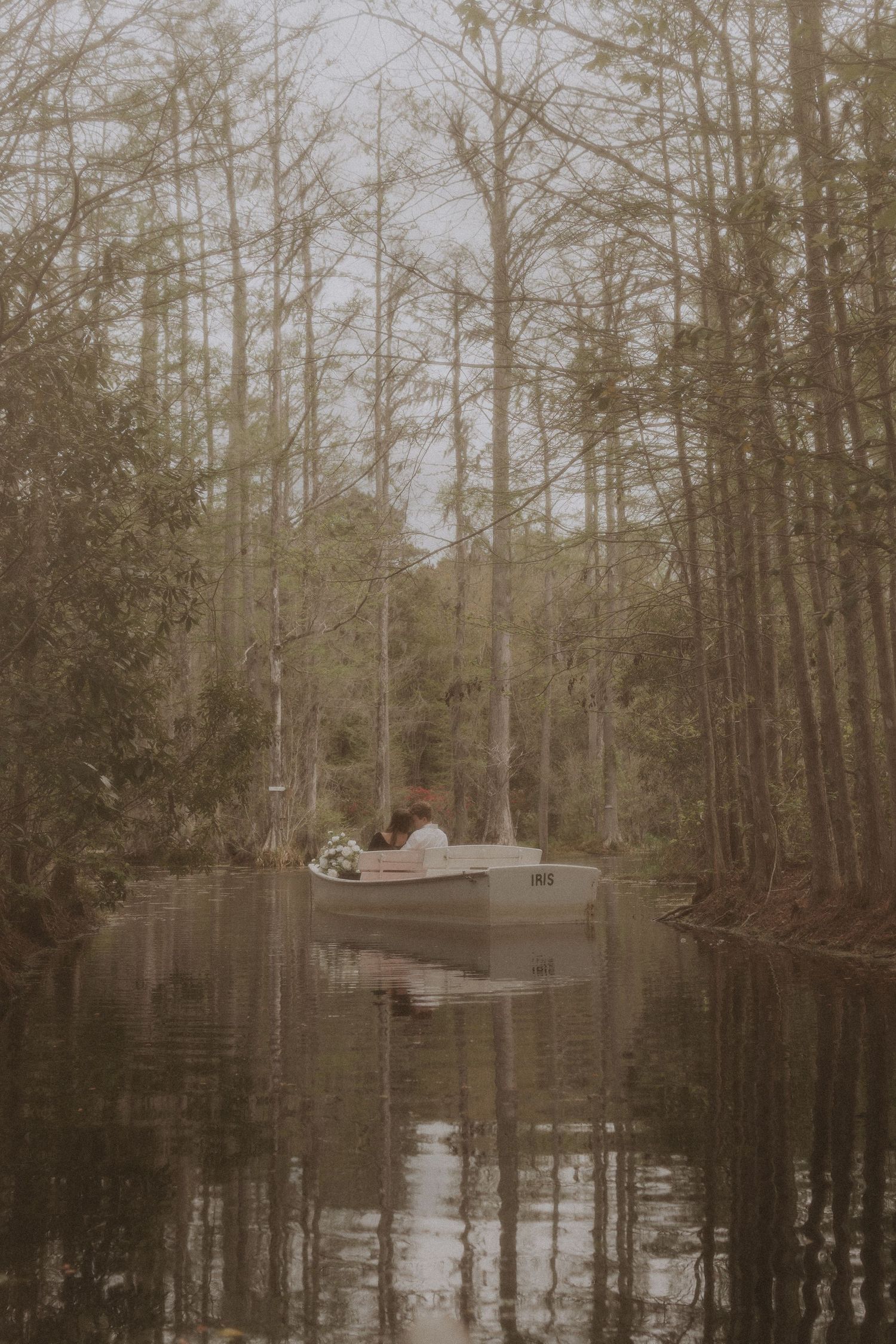 A couple in a canoe at misty swamp landscape with cypress trees reflected in still water.
