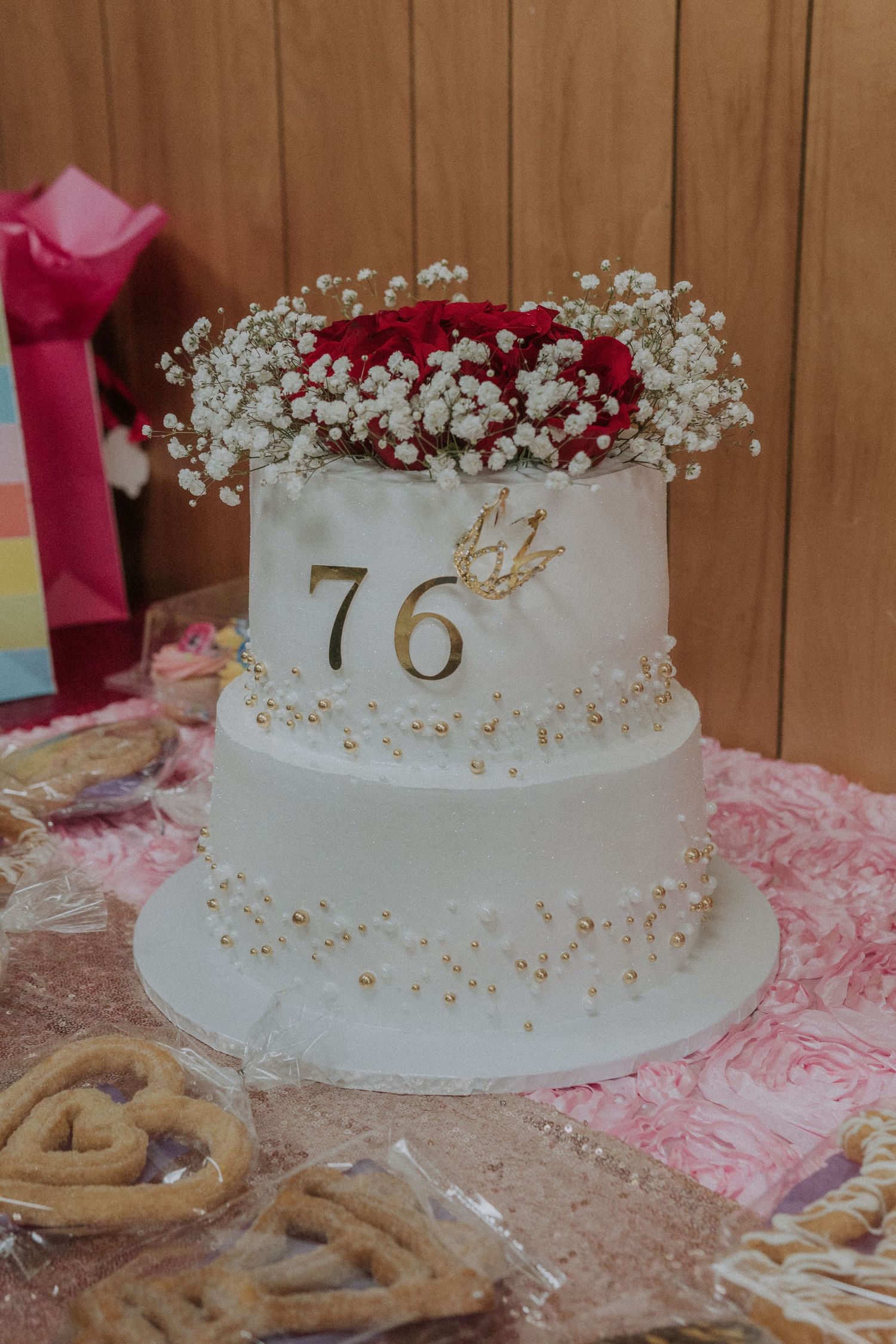Elegant white tiered cake adorned with red roses and gold number 76 on display.