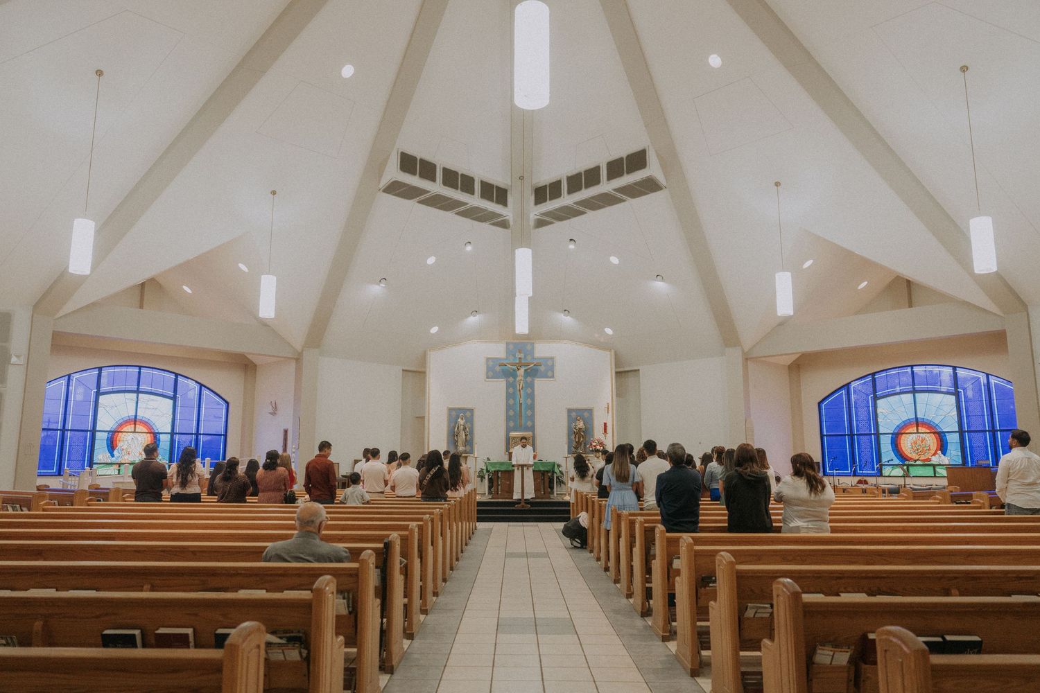 Modern church interior with white vaulted ceiling, wooden pews, and stained glass windows.