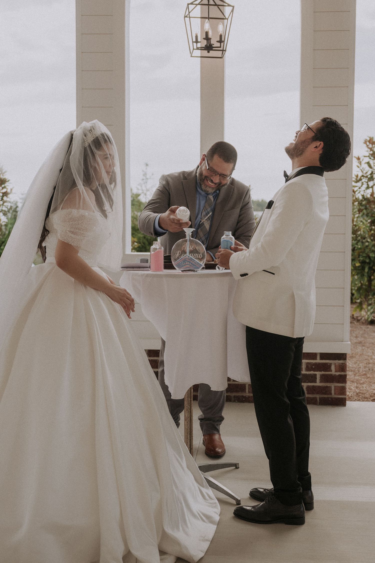 Bride and groom stand at wedding altar during sand ceremony while officiant pours sand into vase.